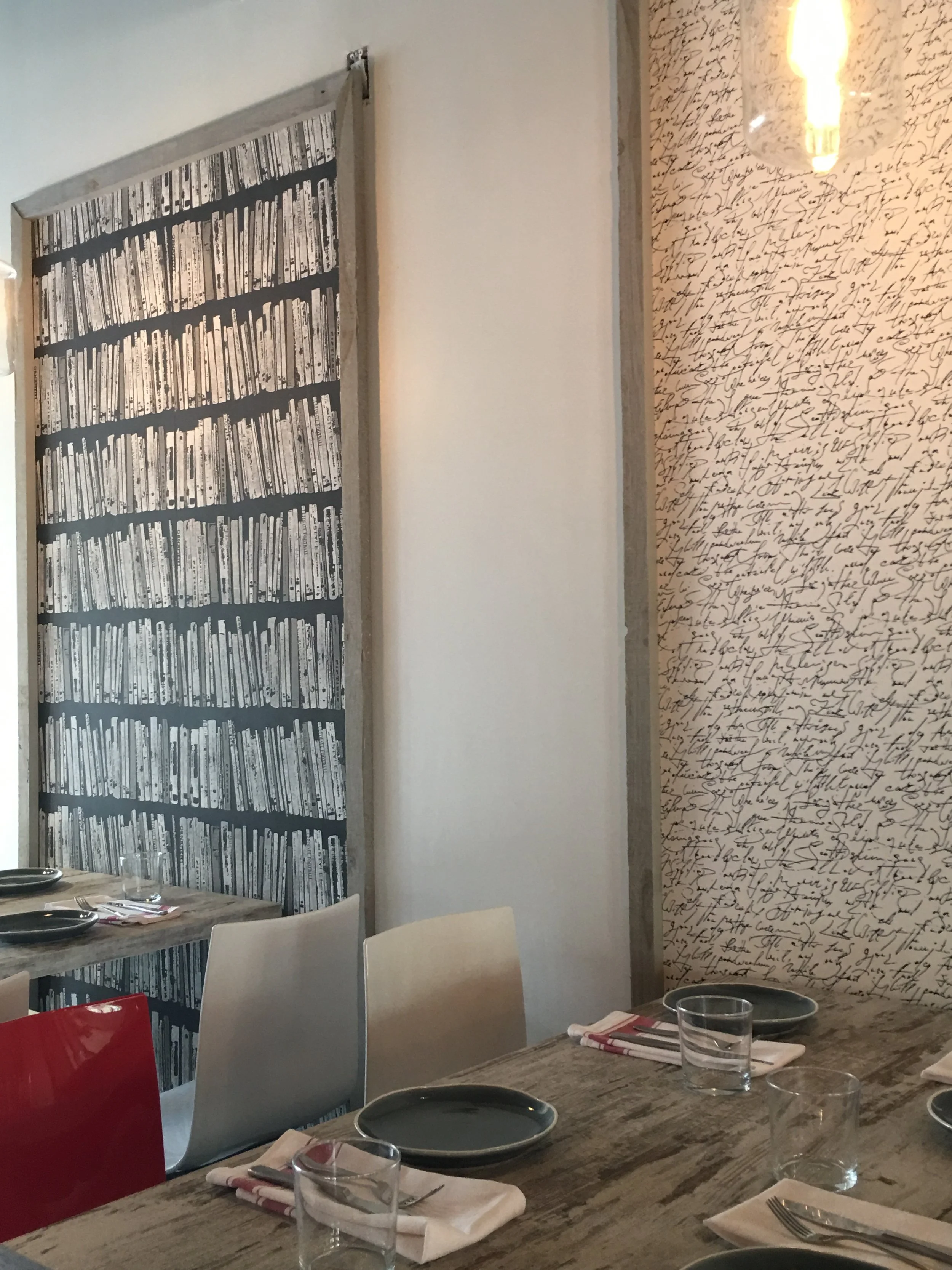 Artistic wall decor with bookshelf and handwriting wallpaper in the intimate dining section of Next Door Restaurant.