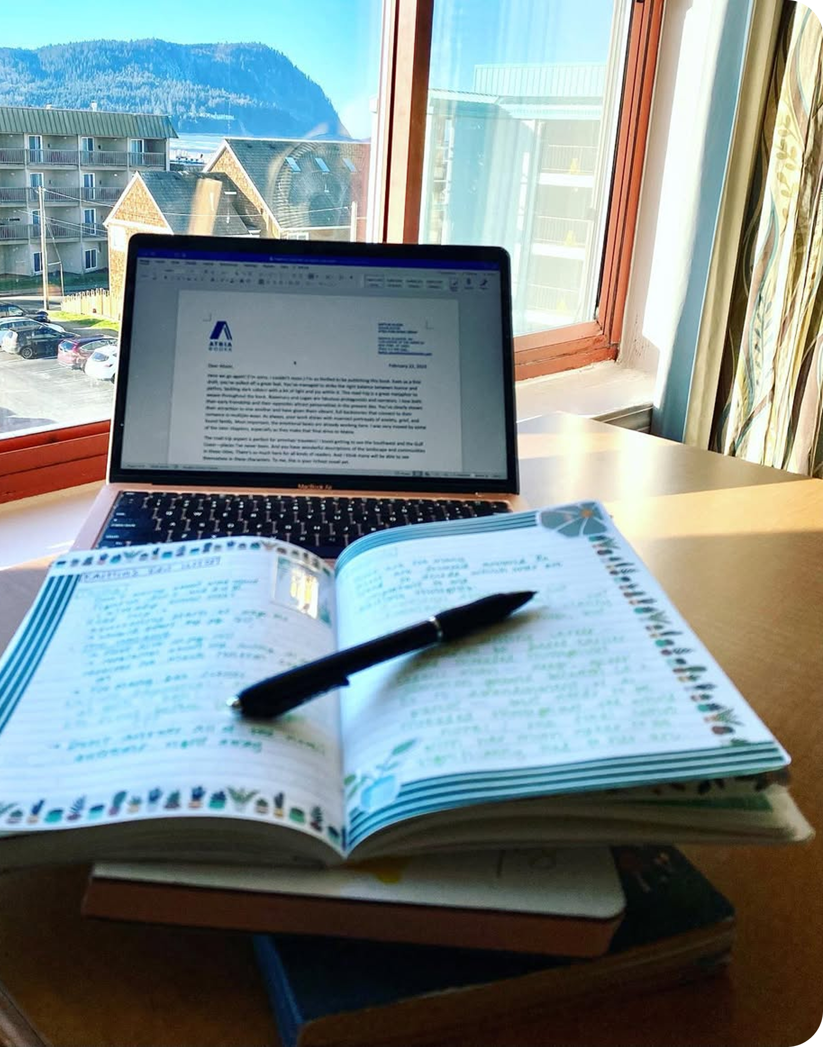 notebook and laptop in front of a picturesque window with a mountain and apartment building