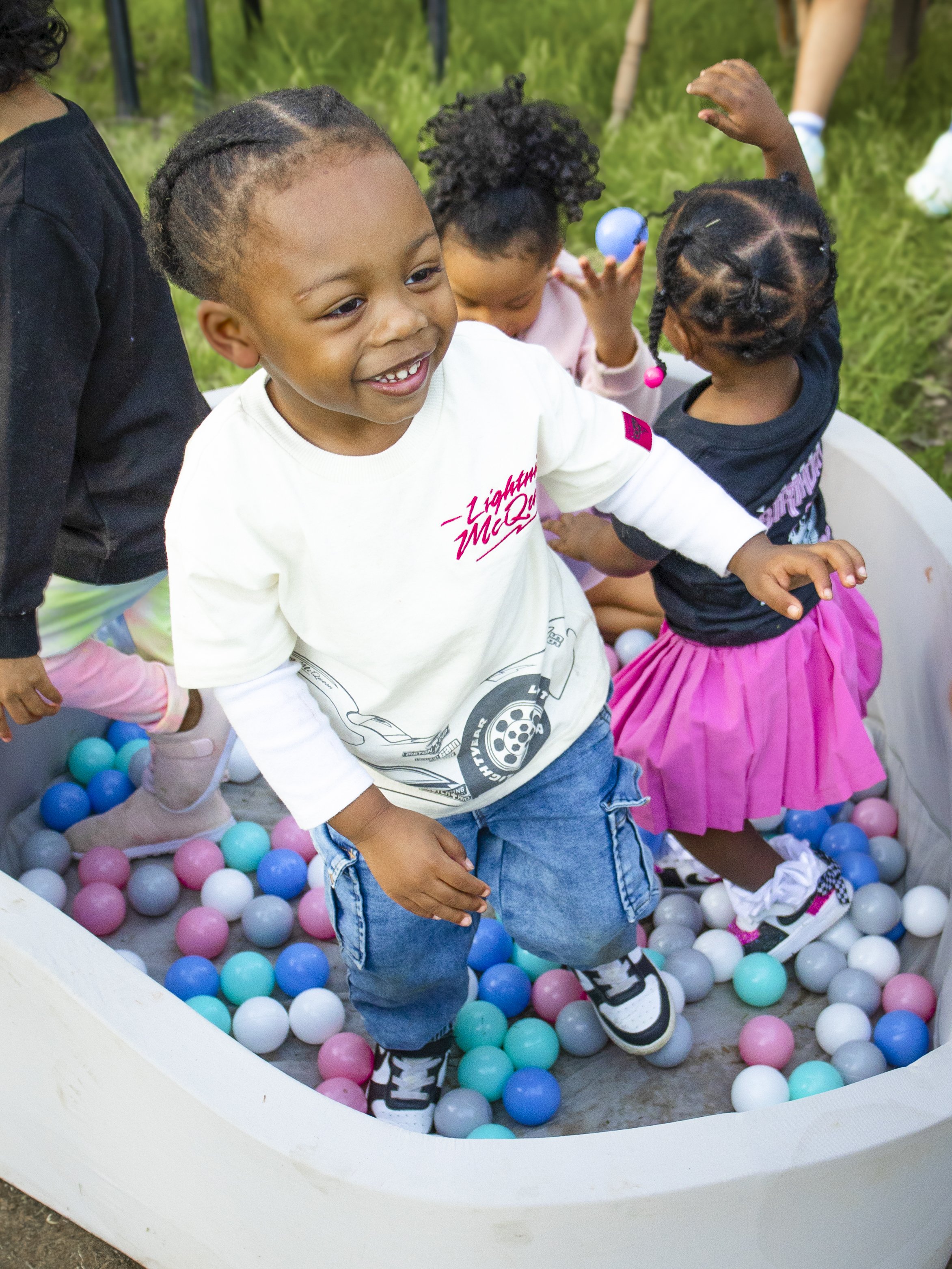 Children playing in a ball pit outdoors with colorful plastic balls, smiling and having fun. Image by Maryland family photographer.