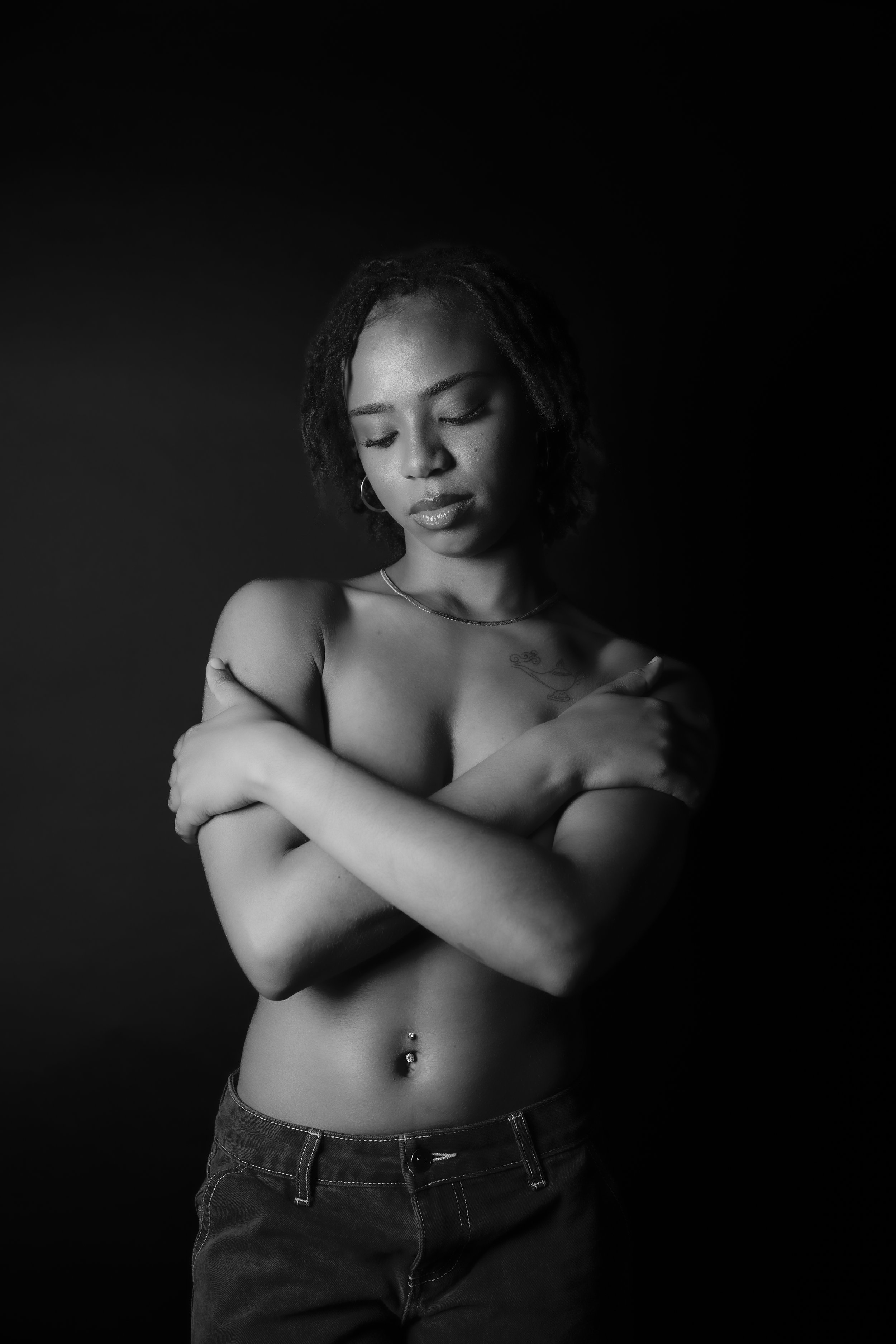 Black and white studio portrait of a person with short hair posing with crossed arms, gazing down.
