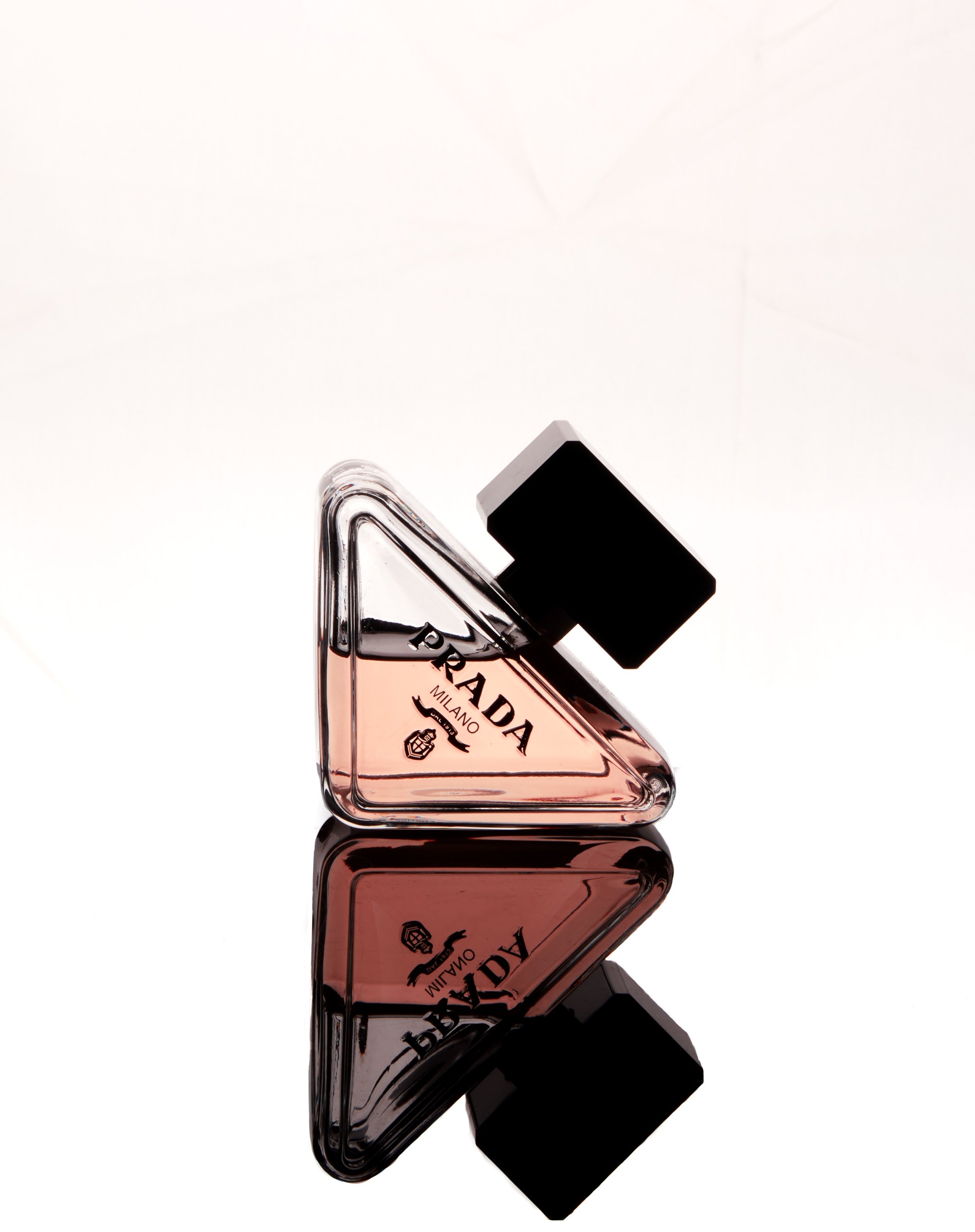 Triangular Prada perfume bottle with black cap, reflected on white surface. Image by Maryland product photographer