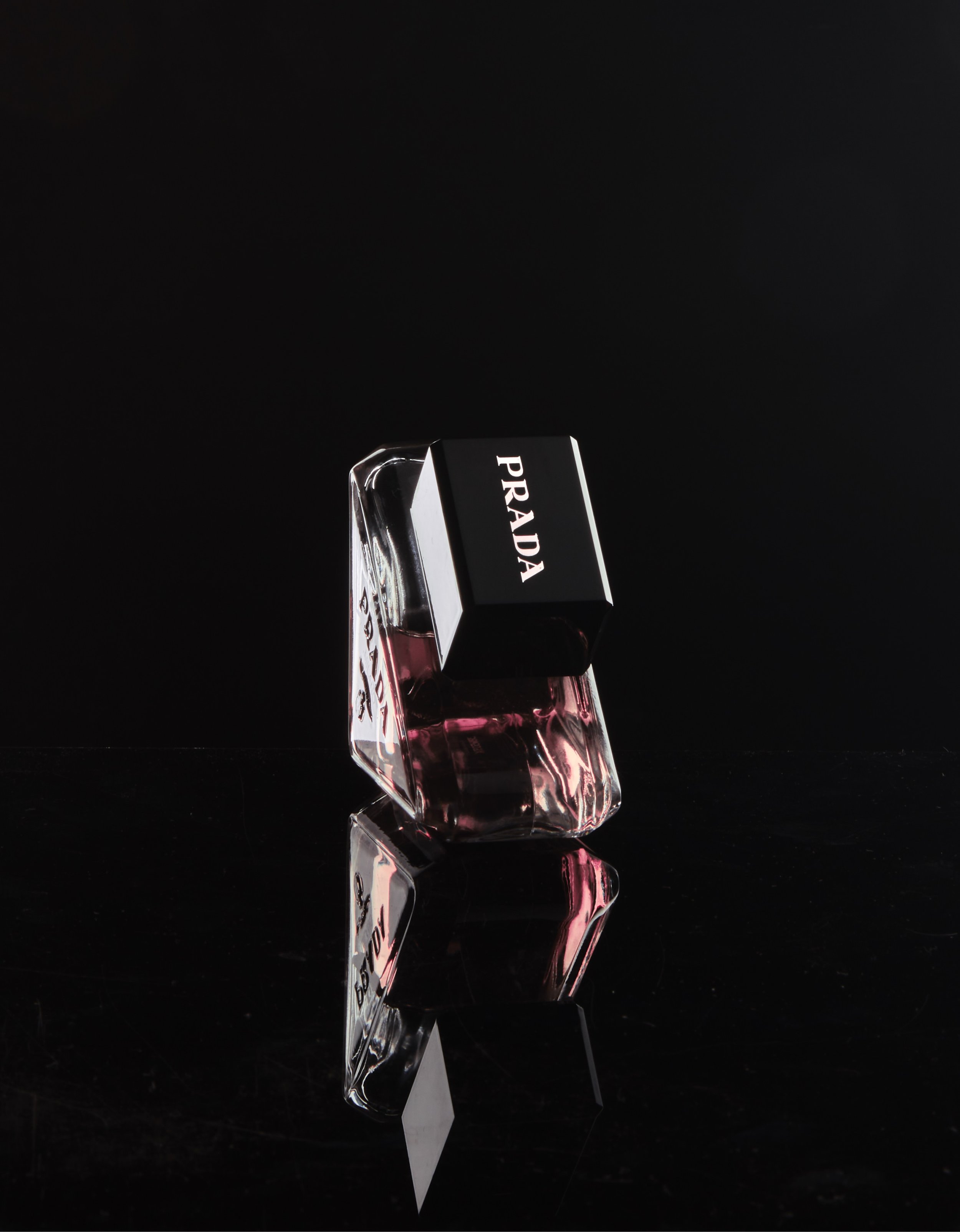 Prada perfume bottle with black cap on a reflective surface, against a dark background. Image by Maryland product photographer.