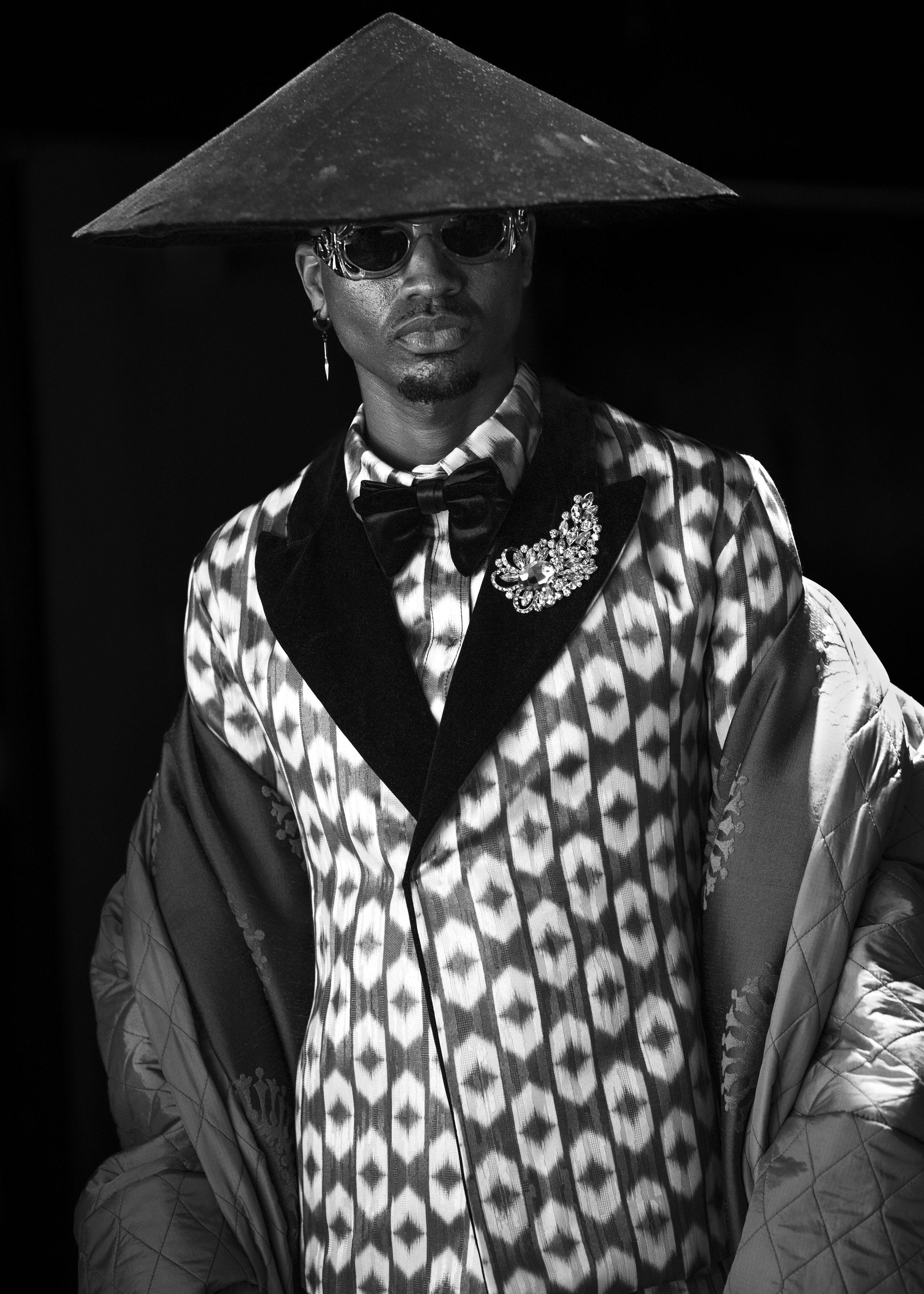 Fashion model wearing a patterned suit, wide-brimmed hat, and sunglasses in black and white photo. Image by portrait photographer.
