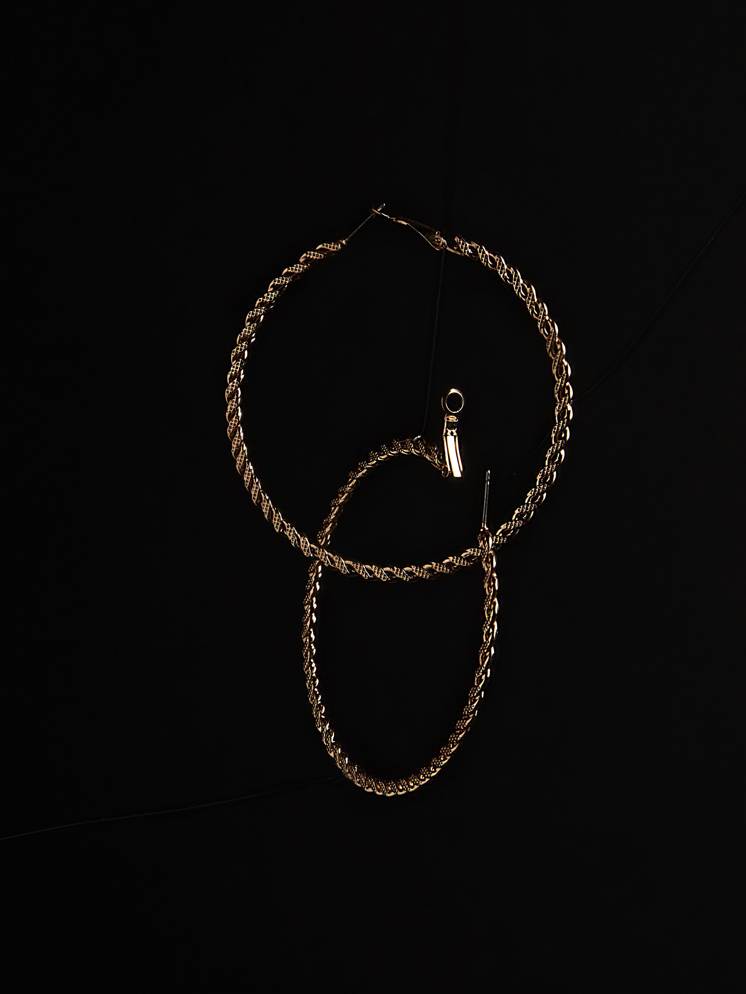DMV area product photographer takes image of gold hoop earrings with a textured design on a black background.