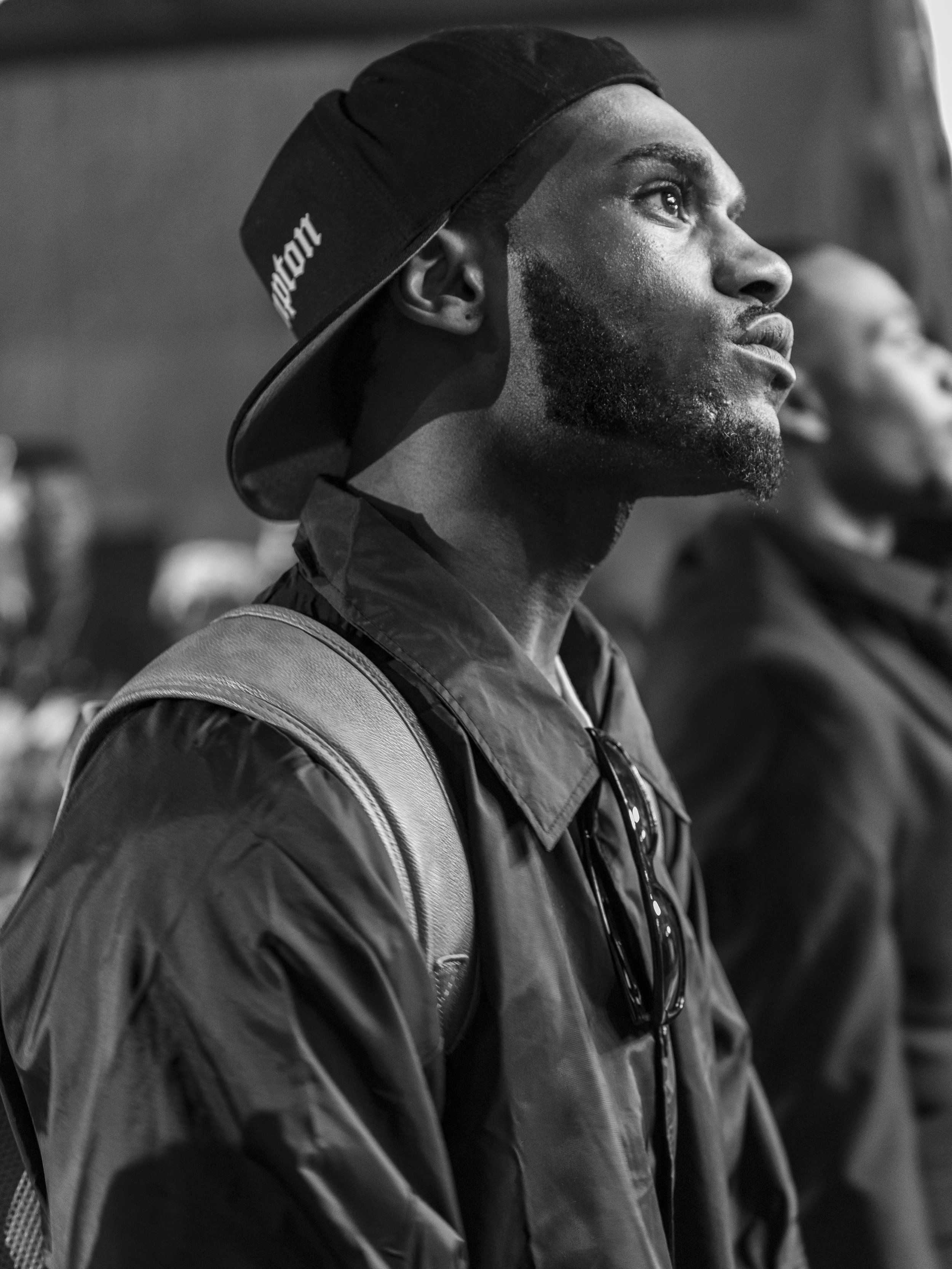 Black and white photo of a man wearing a cap and jacket, looking upwards with a contemplative expression. Image by DMV area event photographer.