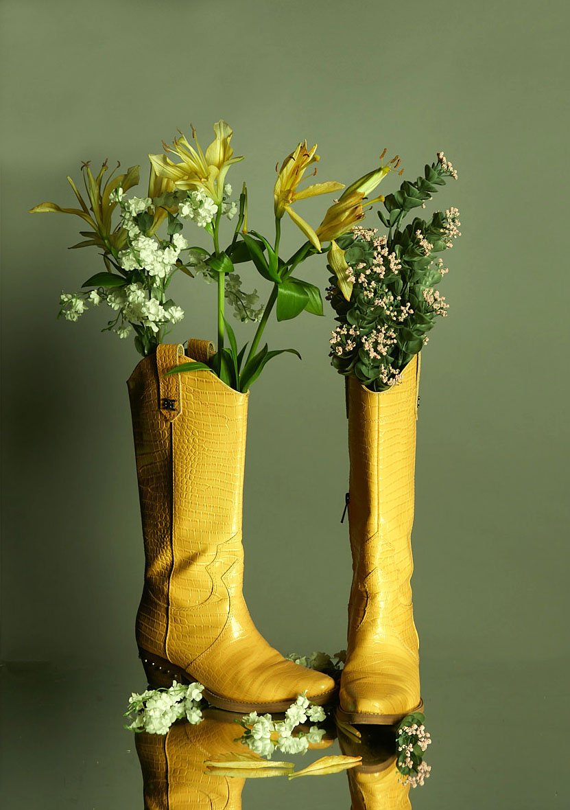 E-Commerce image by product photographer of yellow cowboy boots filled with flowers on reflective surface