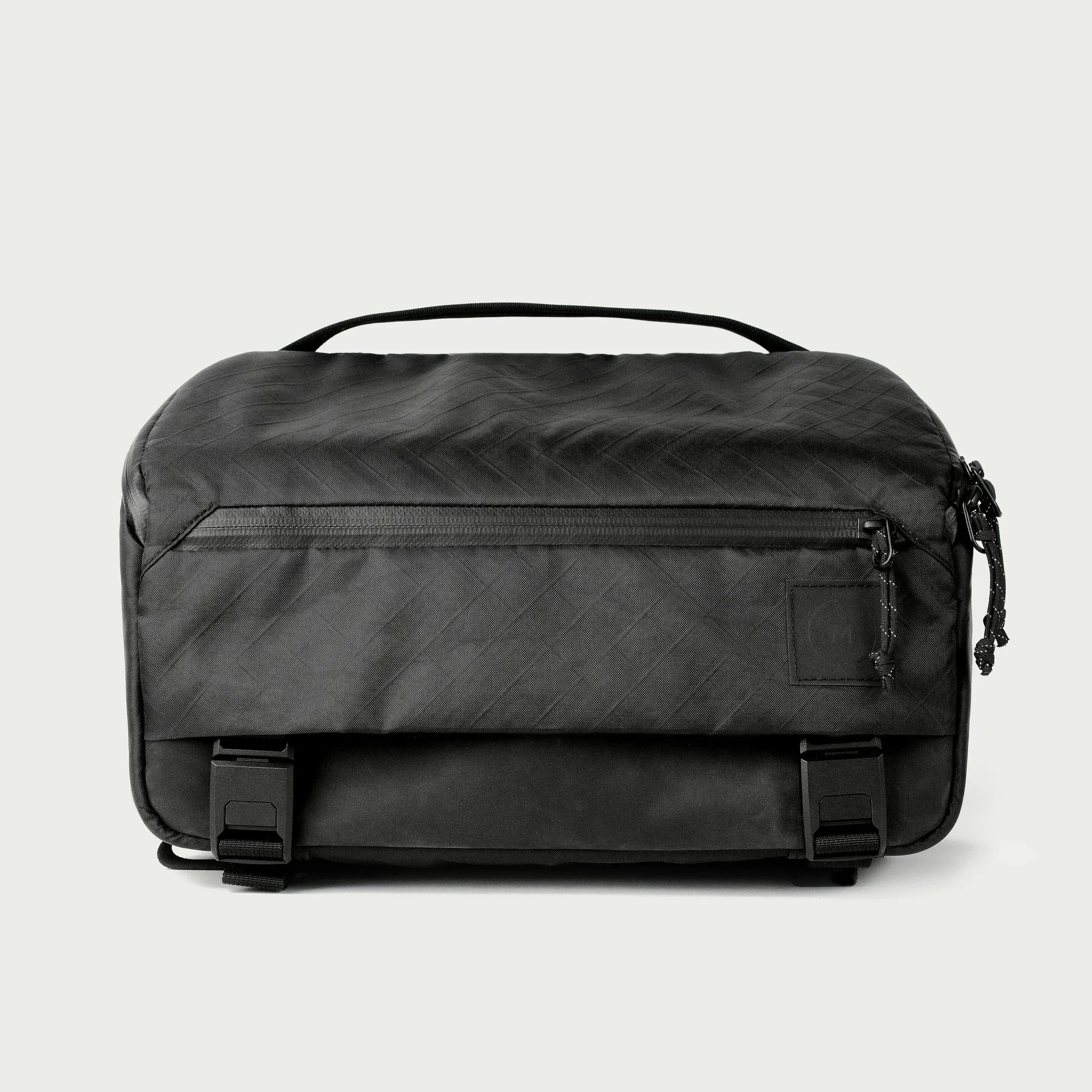 A black zippered bag with textured surface, handle on top, side pocket, and hanging zippers, placed on a white background.