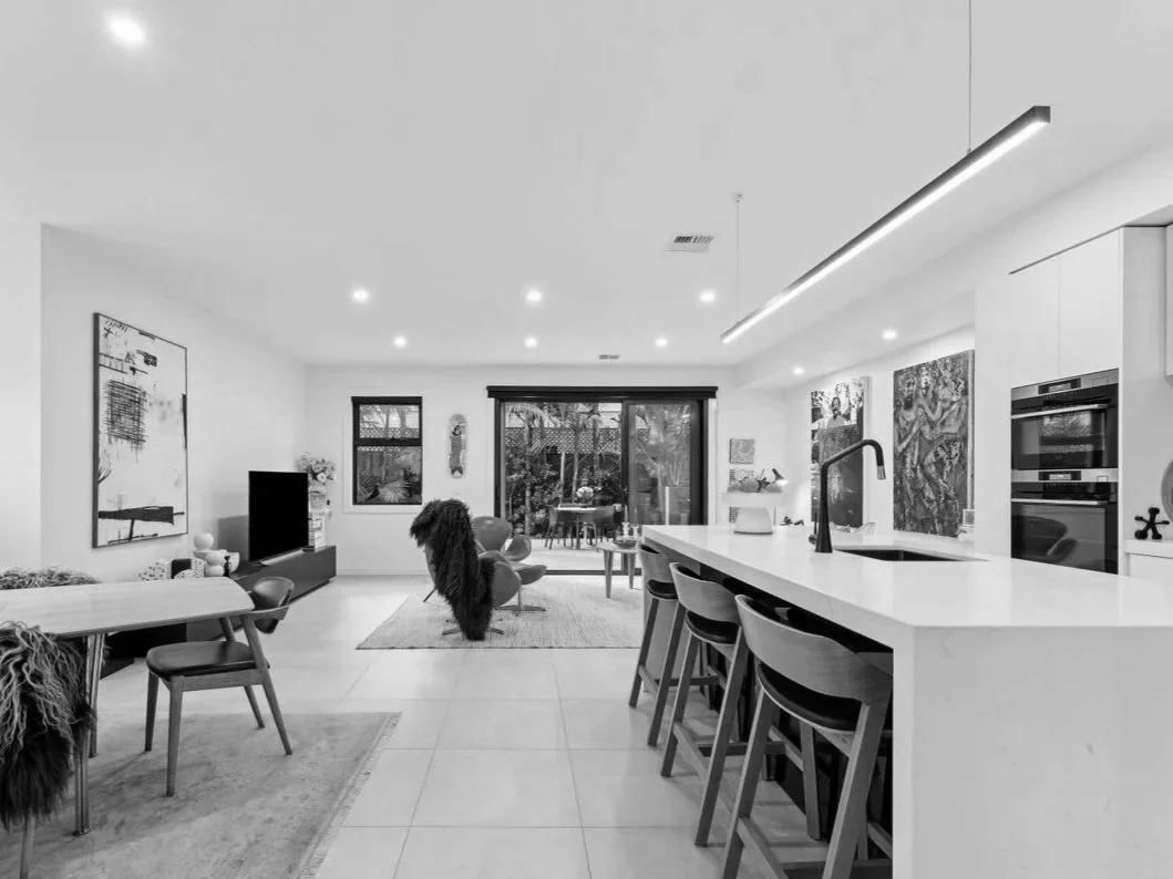 Modern open-concept living room and kitchen with bar seating, artwork, TV, and sliding glass door leading to outdoor patio.