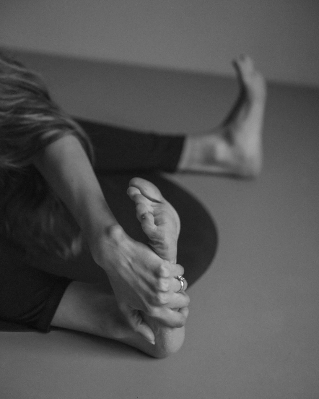 Black and white image of a woman sitting on the floor stretching her legs.