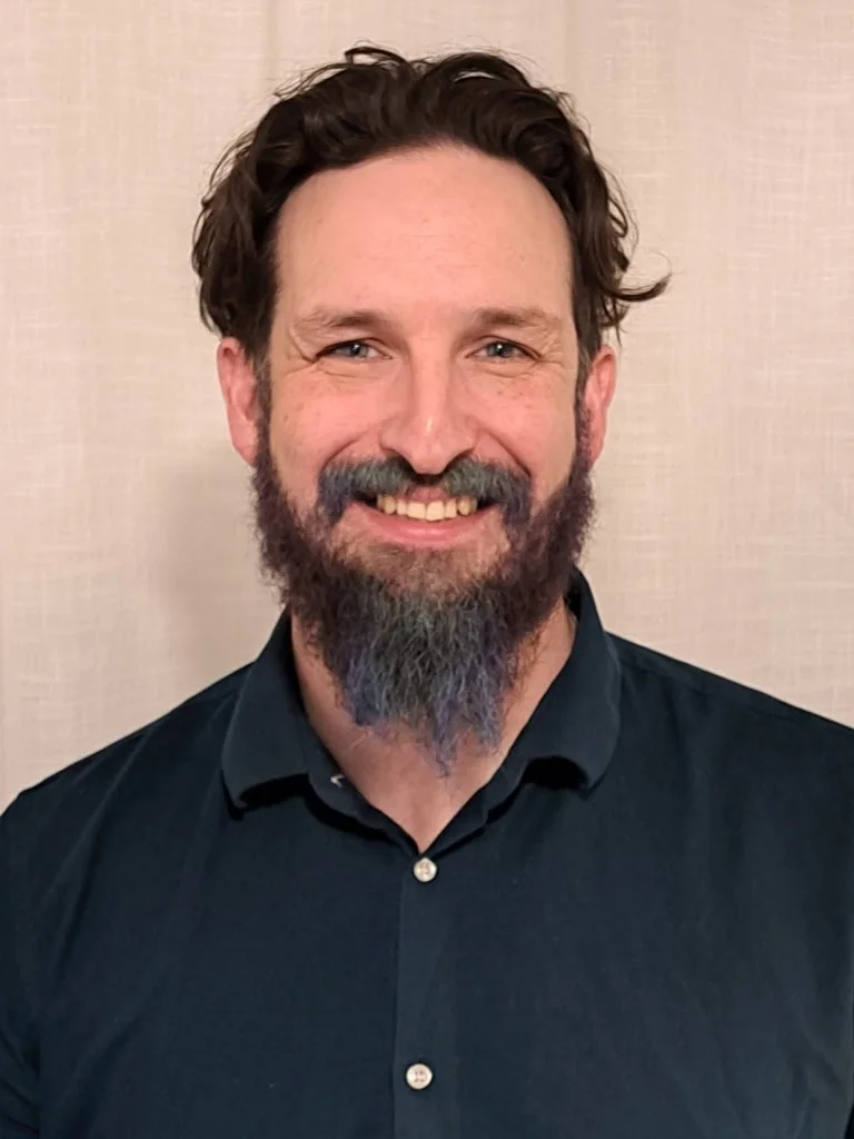 Acupuncturist Dr Steve, a smiling man with dark hair, a beard that is coloured blue, wearing a dark teal shirt