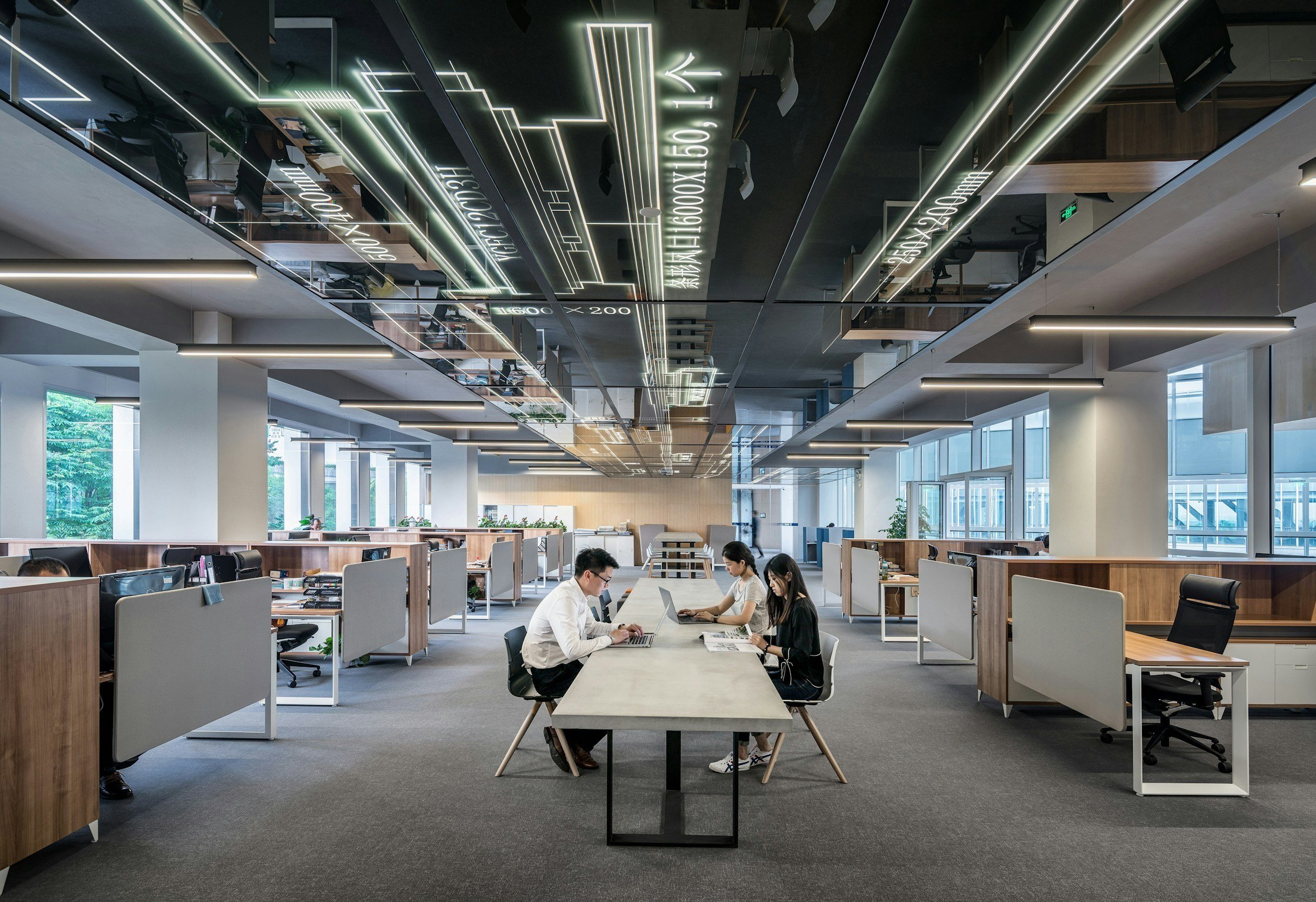 しんさくラボのオフィスの会議室で働く社員3人。シンプルなデザインの長いテーブルと多くの個人用ワークスペース。