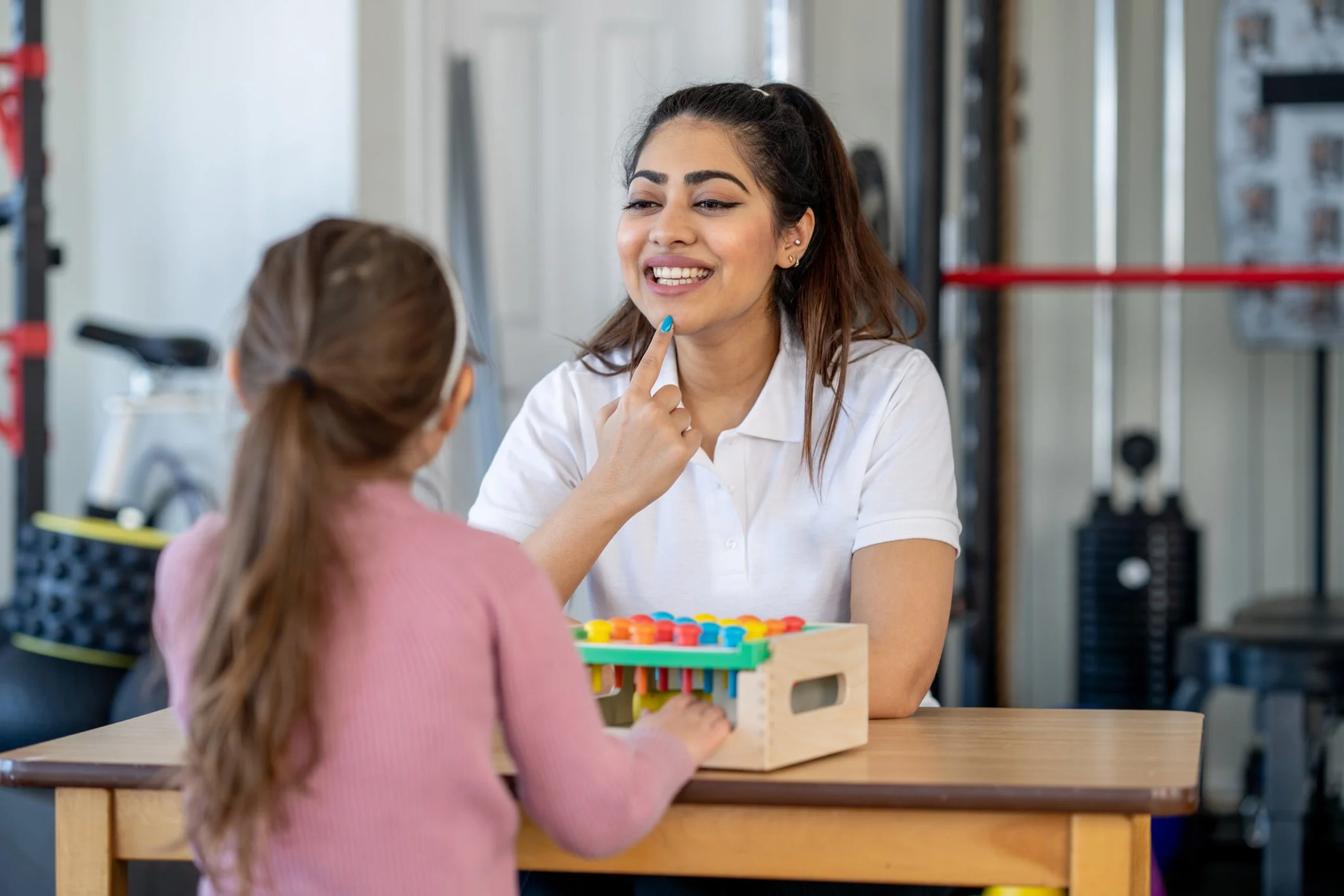 Woman conducting speech therapy with a child in a classroom setting, using a colorful pegboard.