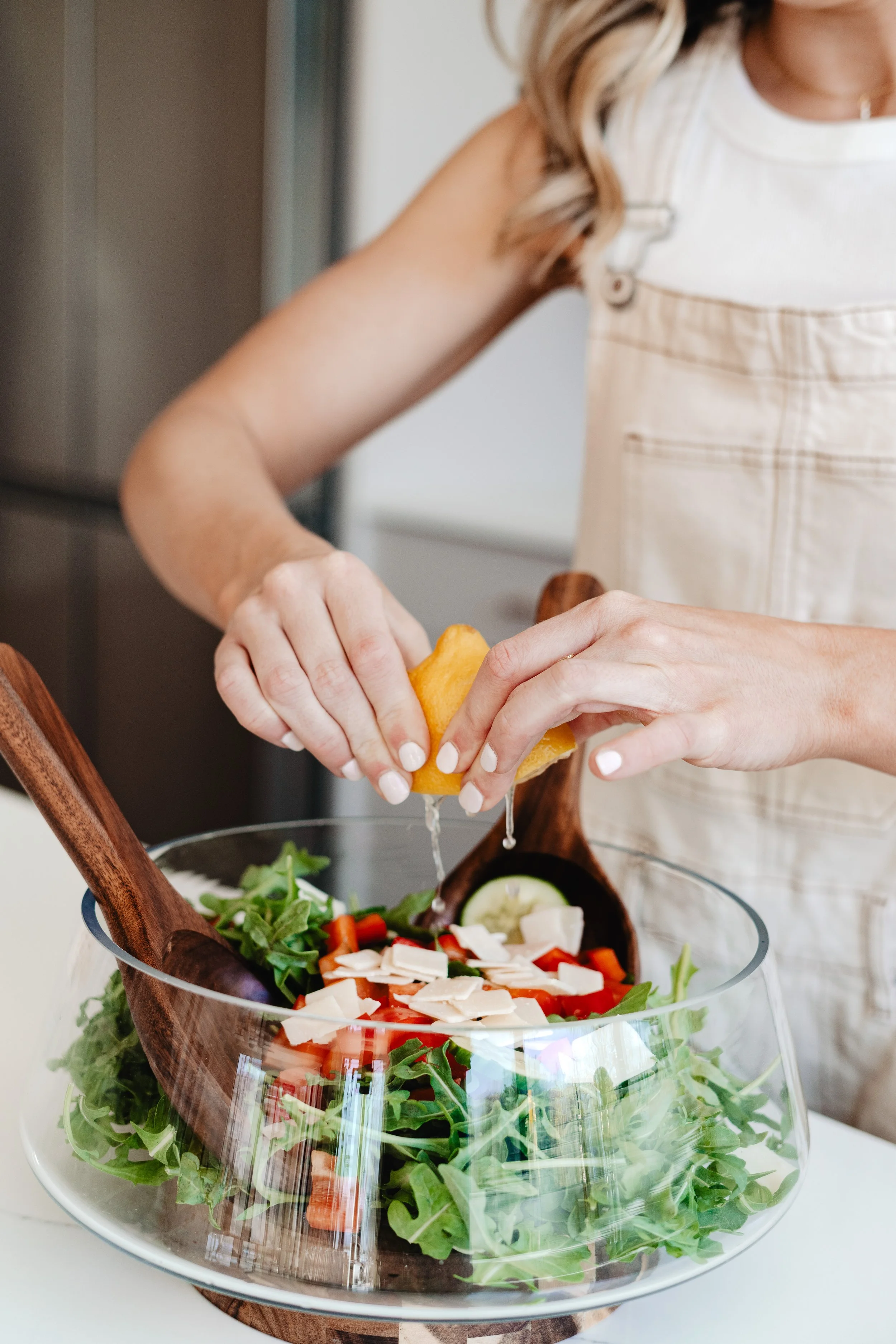 Close-up of a woman fitness and nutritionist expert squeezing lemon into a fresh vegetable salad in a glass bowl for a nutrition app brand shoot in San Diego.