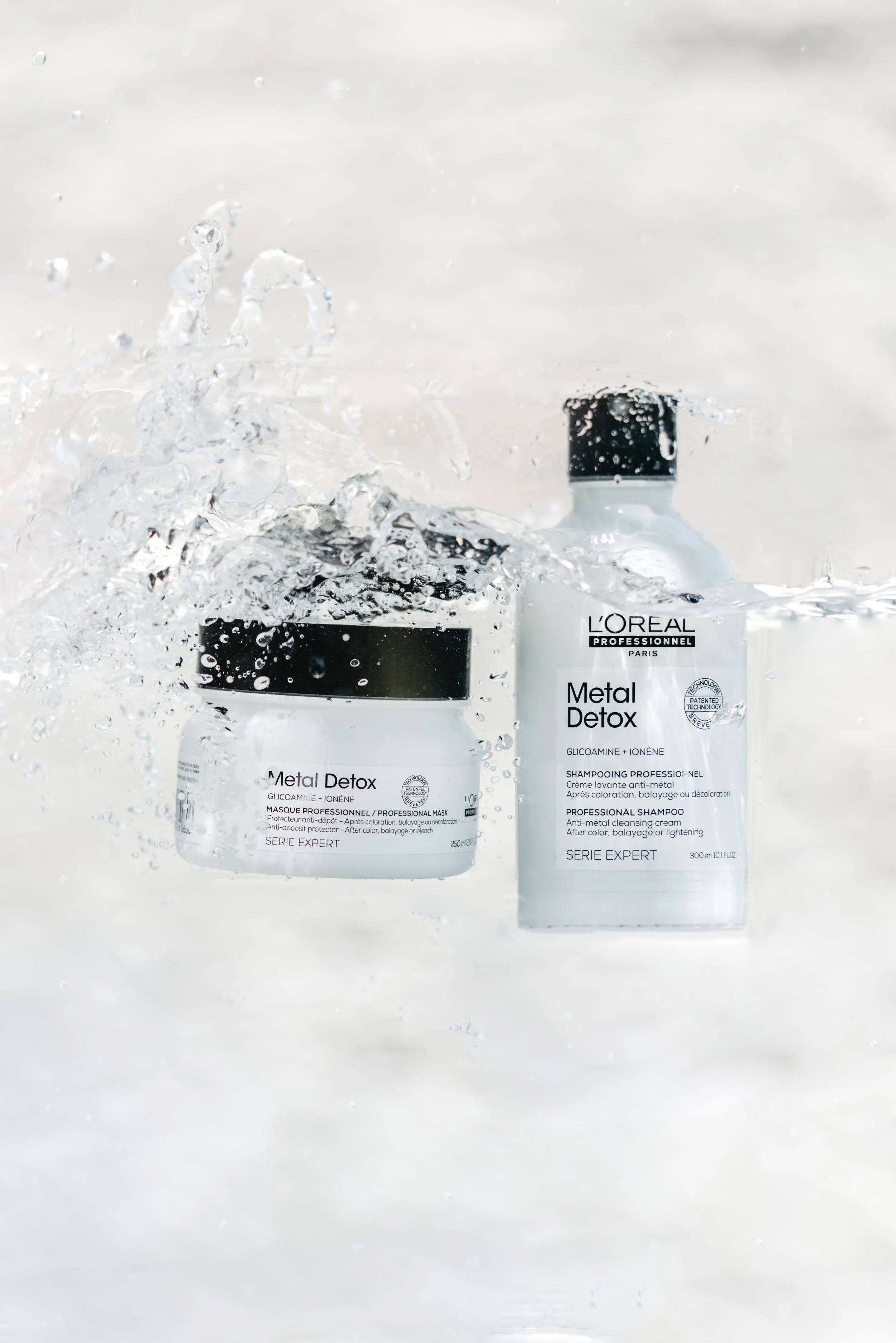 Brand Product photography of two bottles of L'Oreal Professionnel Metal Detox hair care products, one with a black cap and one with a black lid, splash in water with a white background in San Diego 