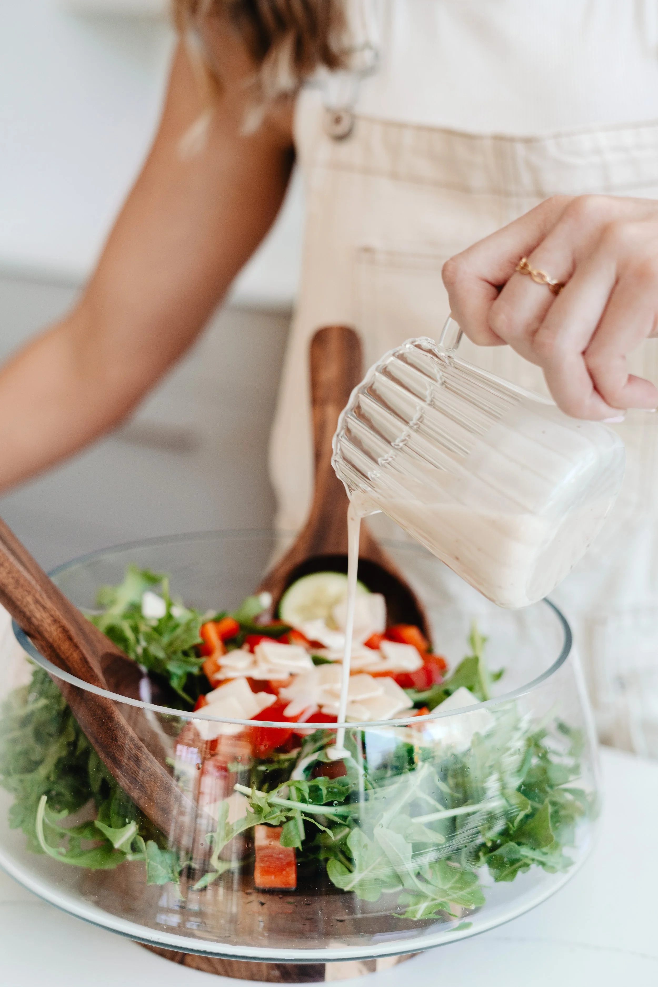Person pouring dressing onto a fresh salad in a glass bowl with vegetables and greens.