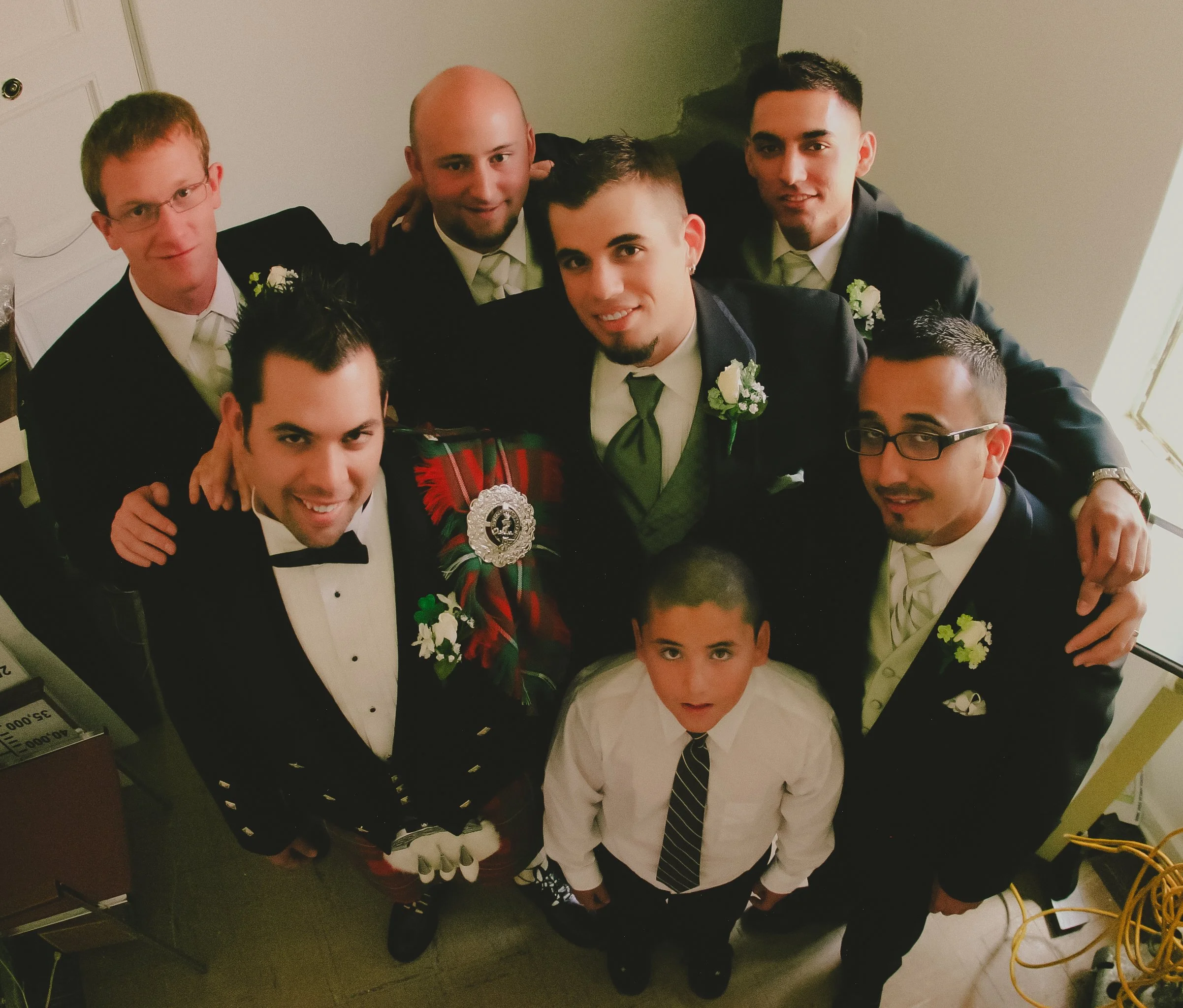 Group of men and a boy dressed in formal wear, gathered together in a small room, looking up at the camera
