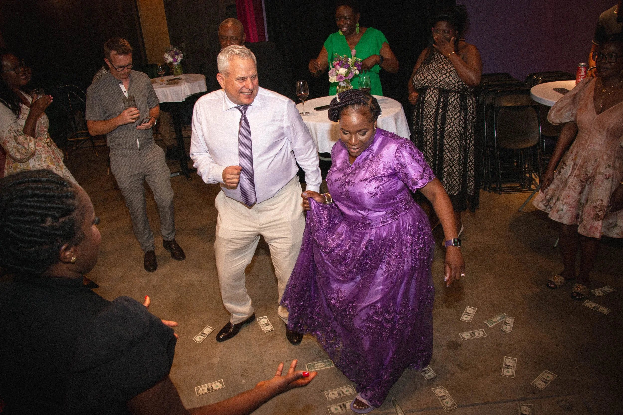 People dancing at a celebration with dollar bills on the floor.