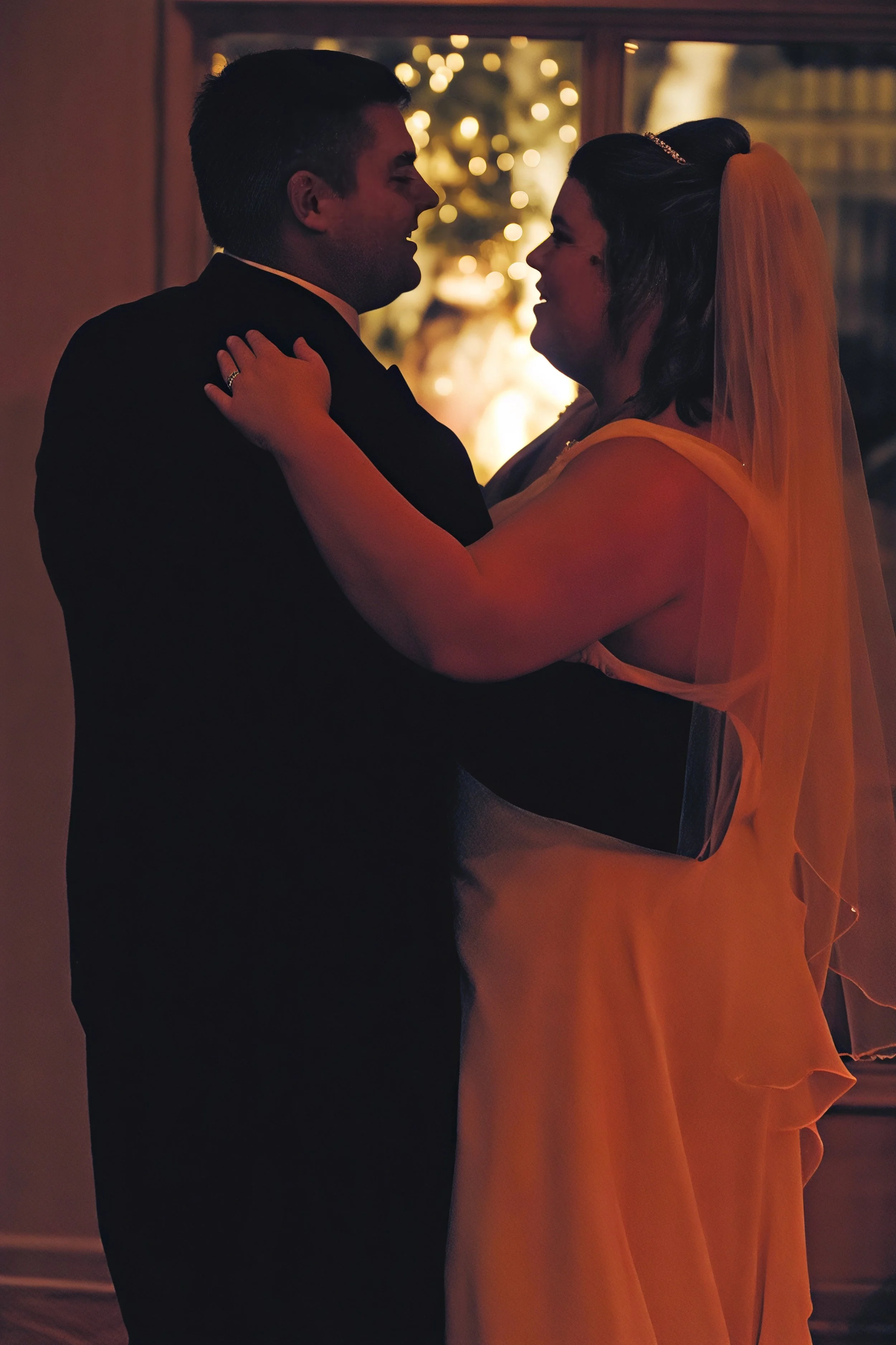 A couple dancing closely in a warmly lit room, with bright decorative lights in the background.