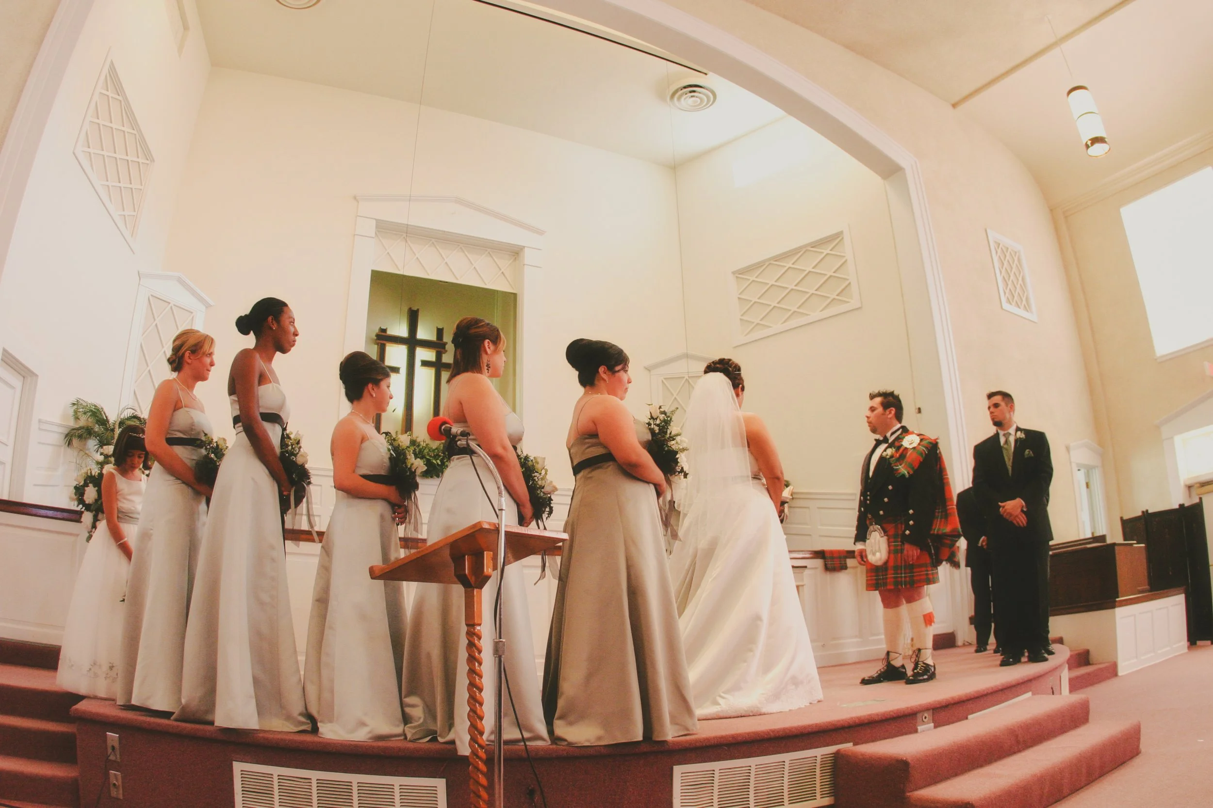 A wedding ceremony taking place in a church, with a bride and groom standing before officiants and bridesmaids in formal dresses.