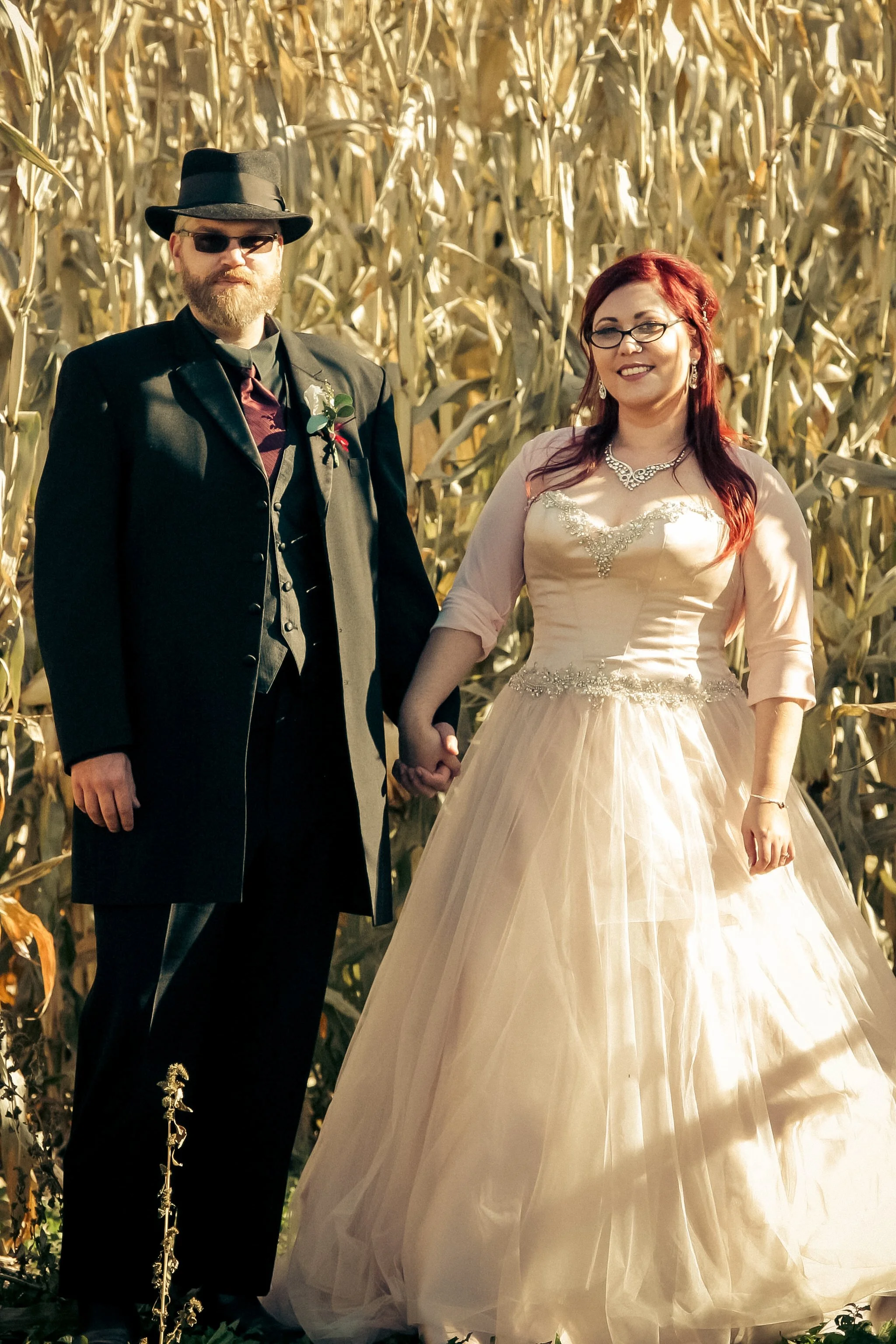 A couple dressed in wedding attire holding hands in a cornfield.