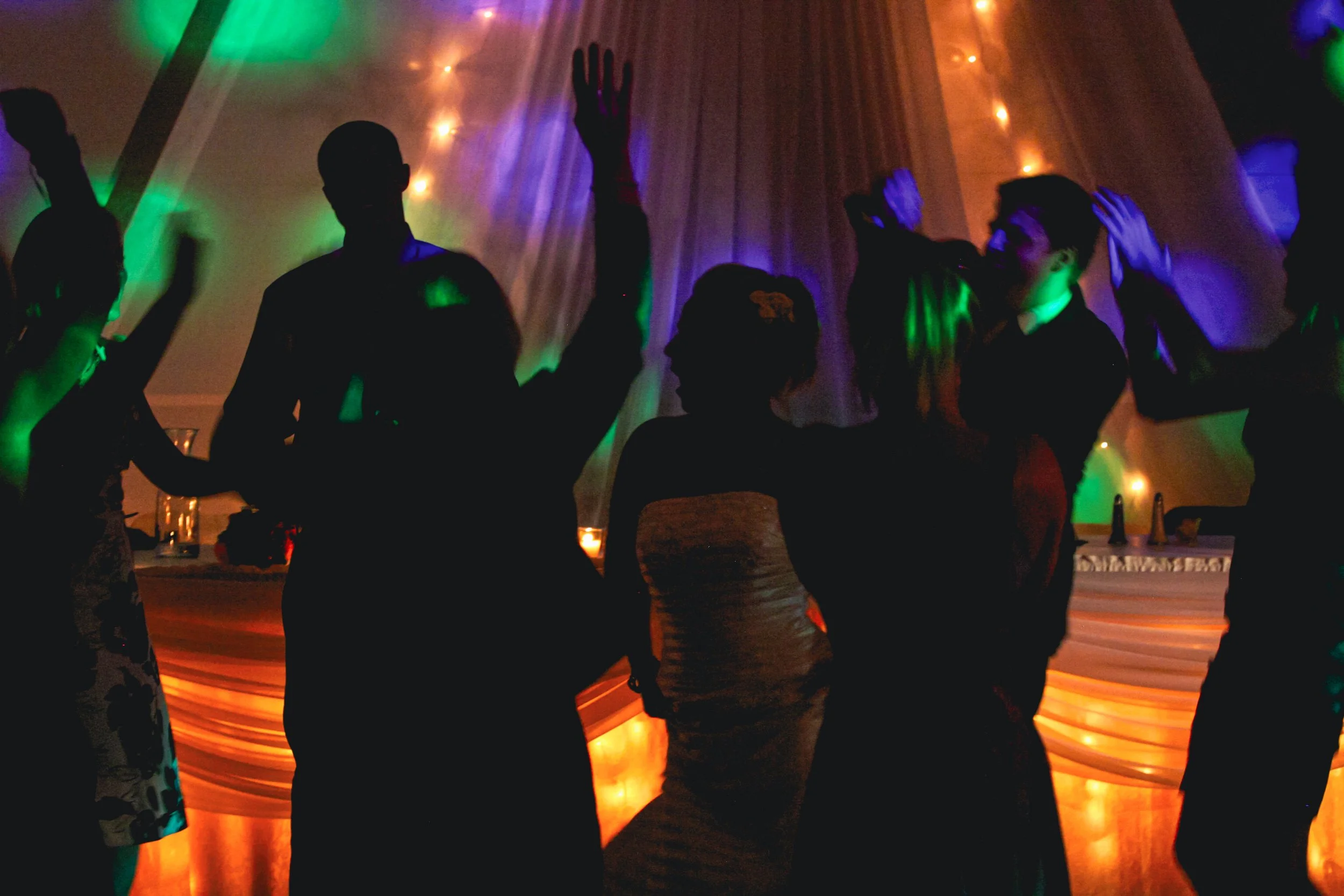 Silhouettes of people dancing and celebrating at a party with colorful lighting.
