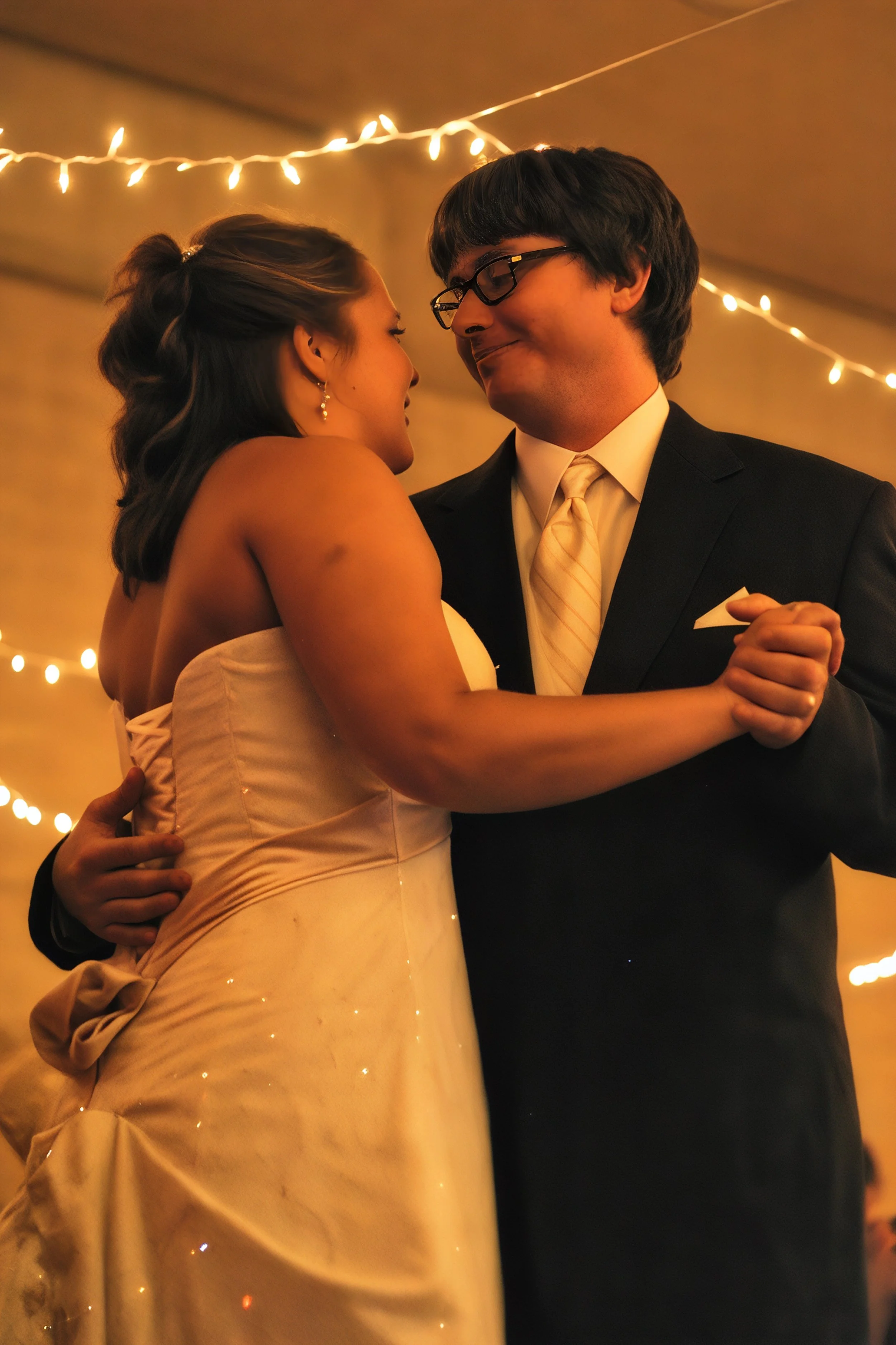 A bride and groom dancing at their wedding reception under warm lighting with string lights in the background.
