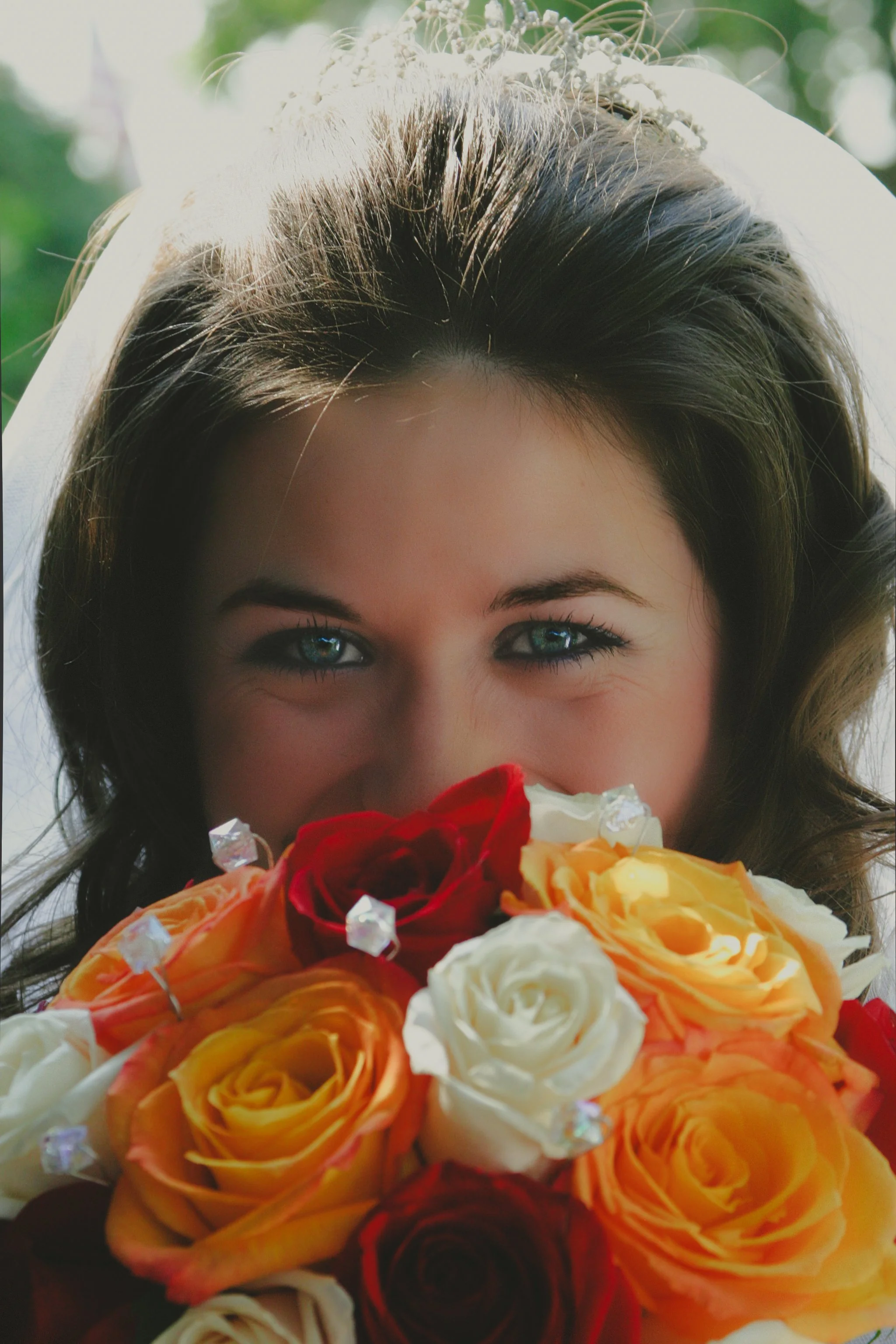 Close-up of a bride with blue eyes holding a bouquet of colorful roses.