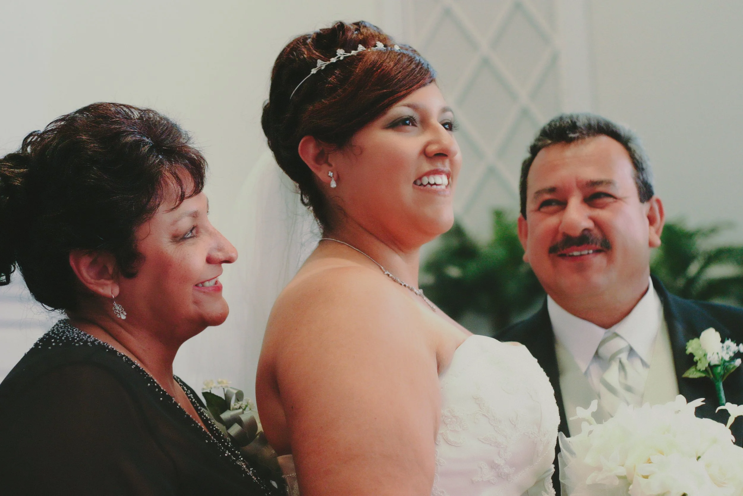 A bride in a wedding dress standing between a woman and a man, all smiling.