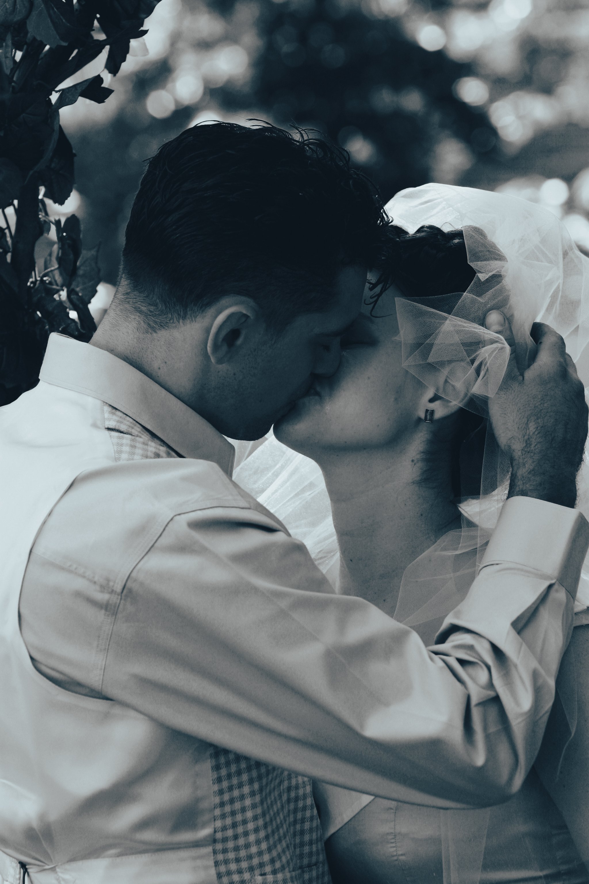 A black-and-white photo of a man and woman sharing a kiss, with the man holding the woman's face, during a wedding.