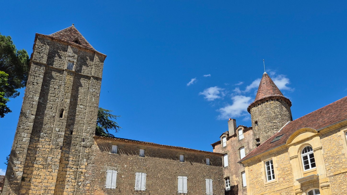belves tour de l'auditoire next to another tower with a pointed spire, the old college of Belves in the foreground with beautiful blue sky and a few clouds.