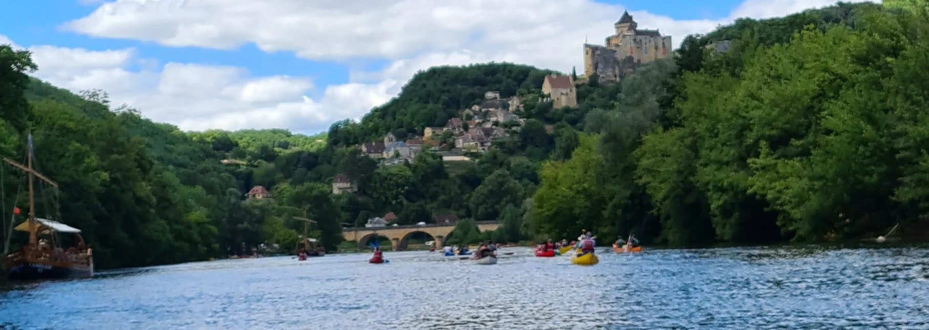 Picture of Castelnaud castle above the dordogne. There is a gabarre and canoes floating on the Dordogne river