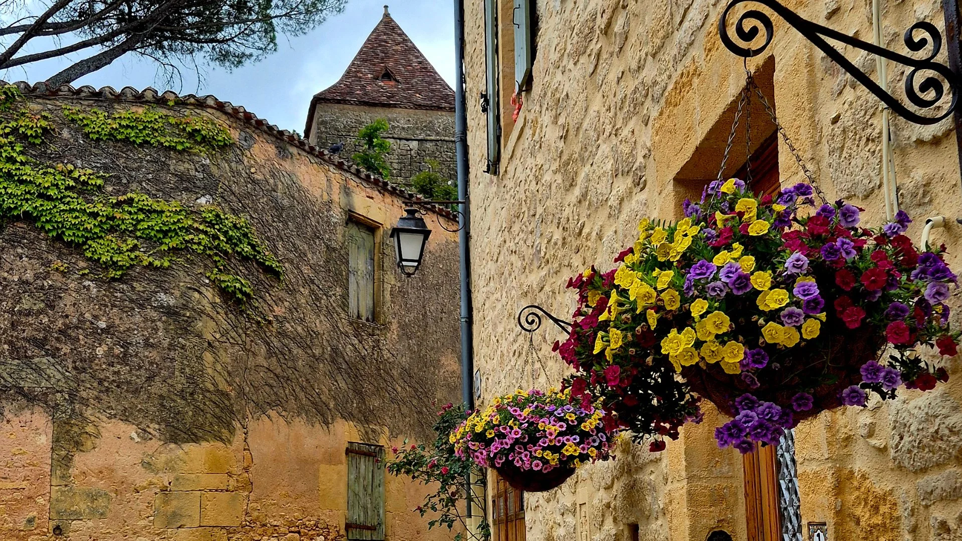medieval building with a flower basket hanging from it, ant the castrum defensive walls infront. Beyond that, you can see a medieval tower