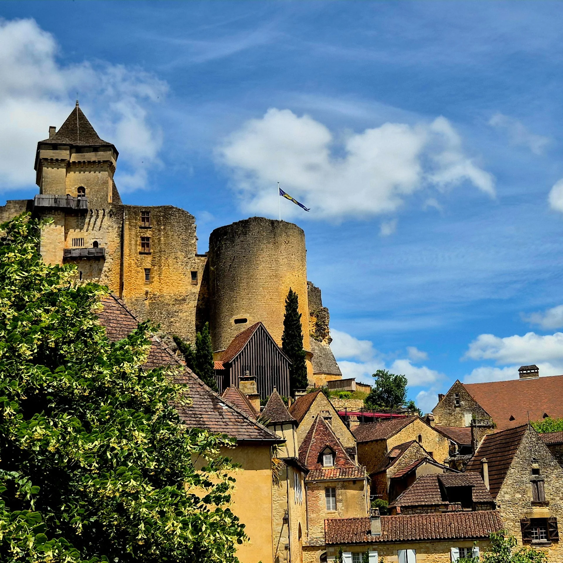 castelnaud village with the castle towering above it with the flag flying