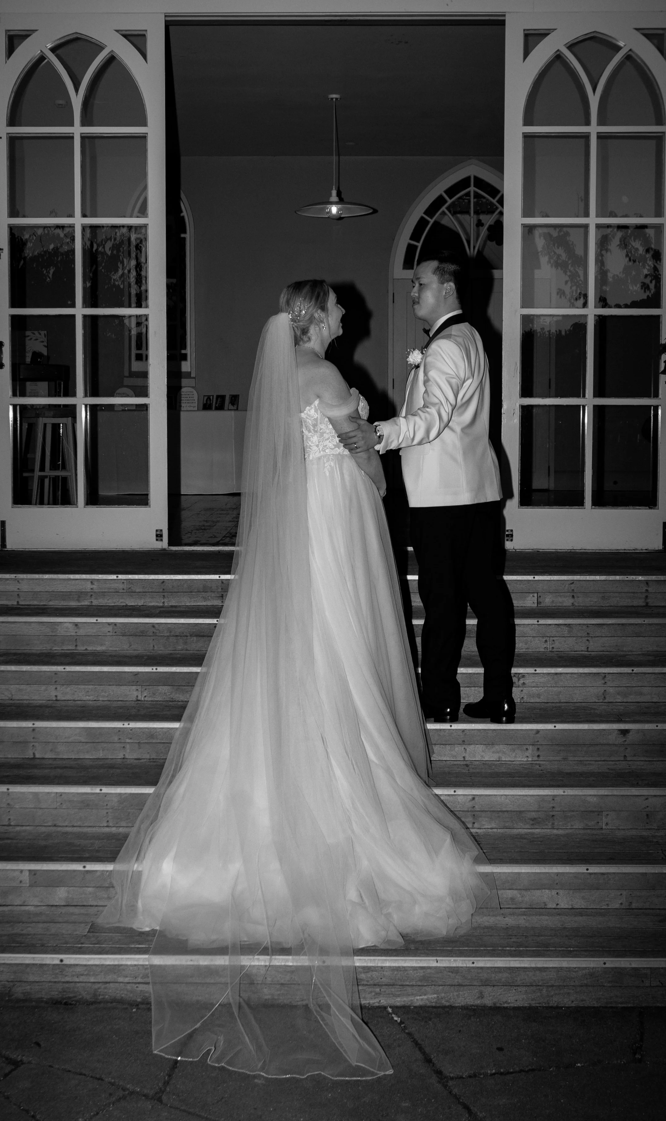 A bride and groom holding hands on the steps outside a building, facing each other during their wedding.