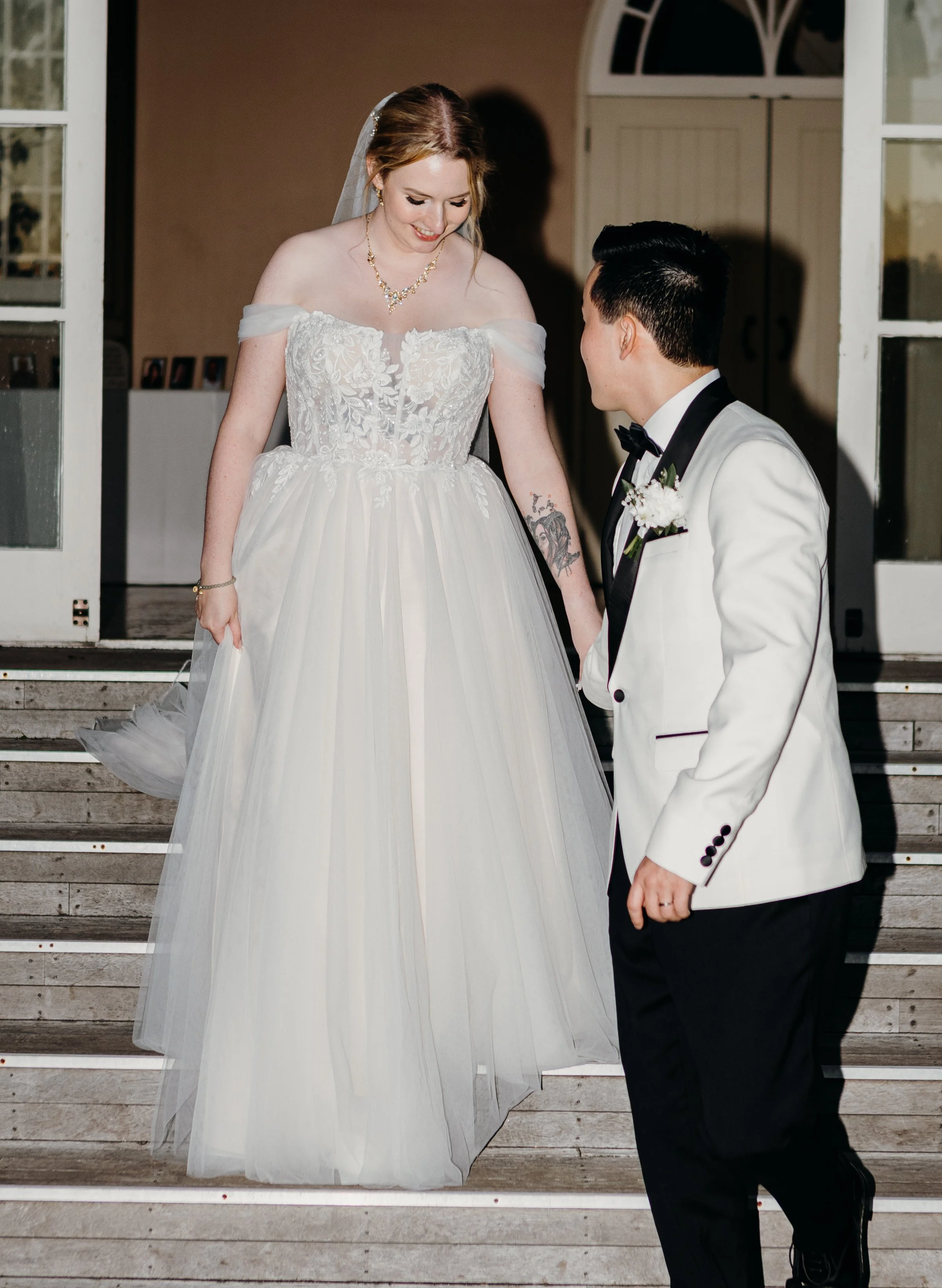 A bride and groom on the steps of a building during their wedding, holding hands and looking at each other.
