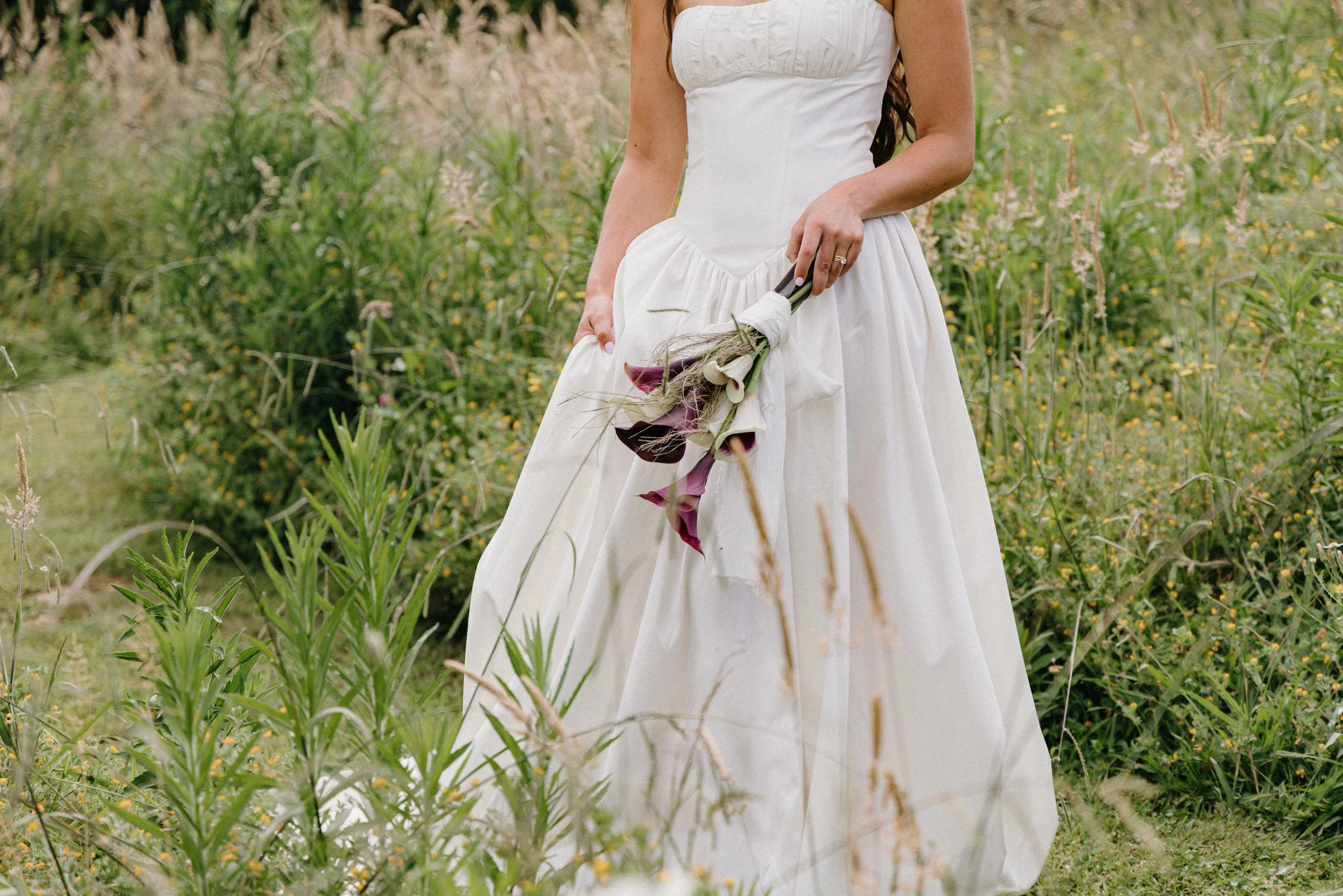 A woman in a white wedding dress holds a bouquet of calla lilies in a field of wildflowers.
