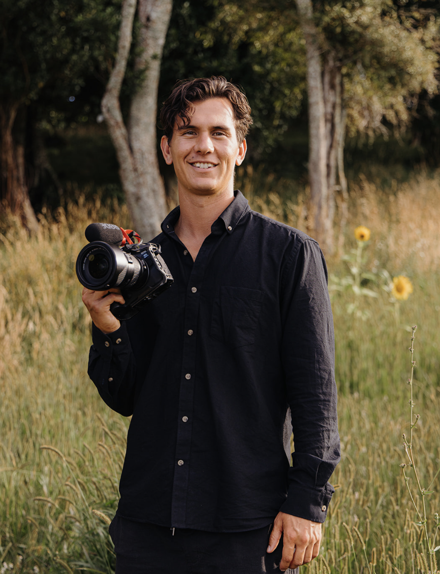 Kahu Tataurangi, wedding videographer at The Wedding Photographers NZ, holding a camera outdoors in the Bay of Plenty.