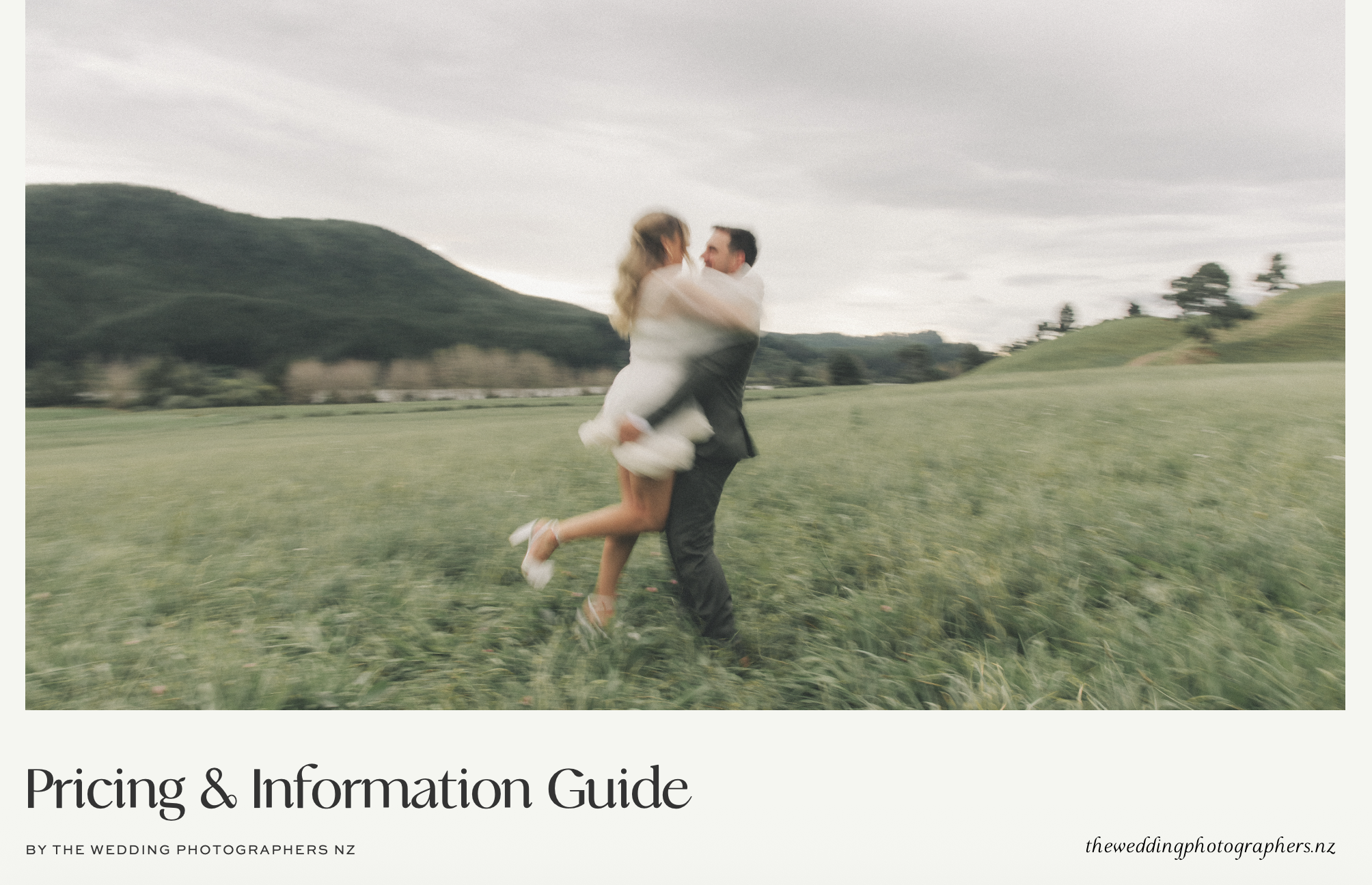 A couple in wedding attire hugging and spinning in a green field with mountains in the background.