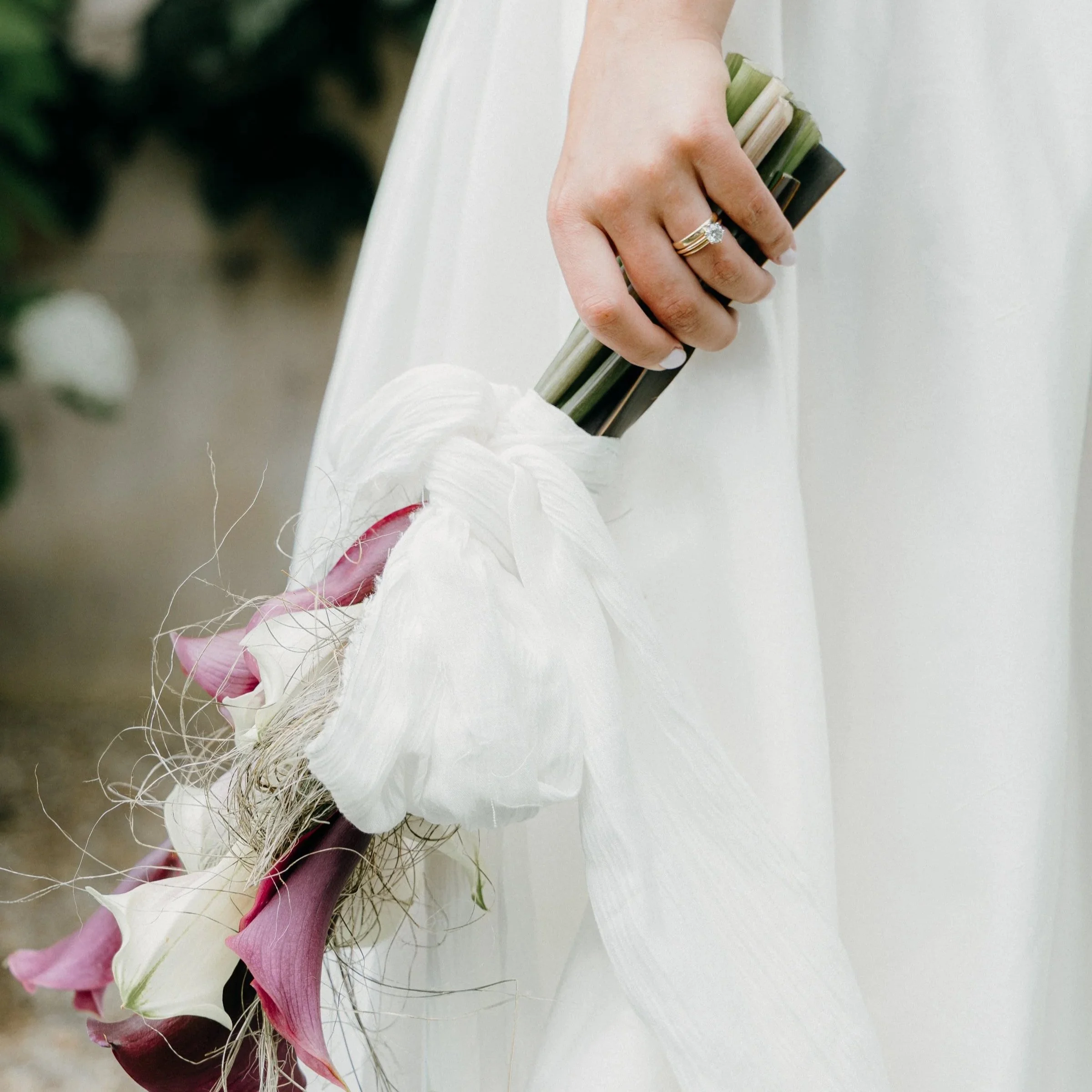 A person in a white dress holding a bouquet of flowers with a wedding ring on their finger.