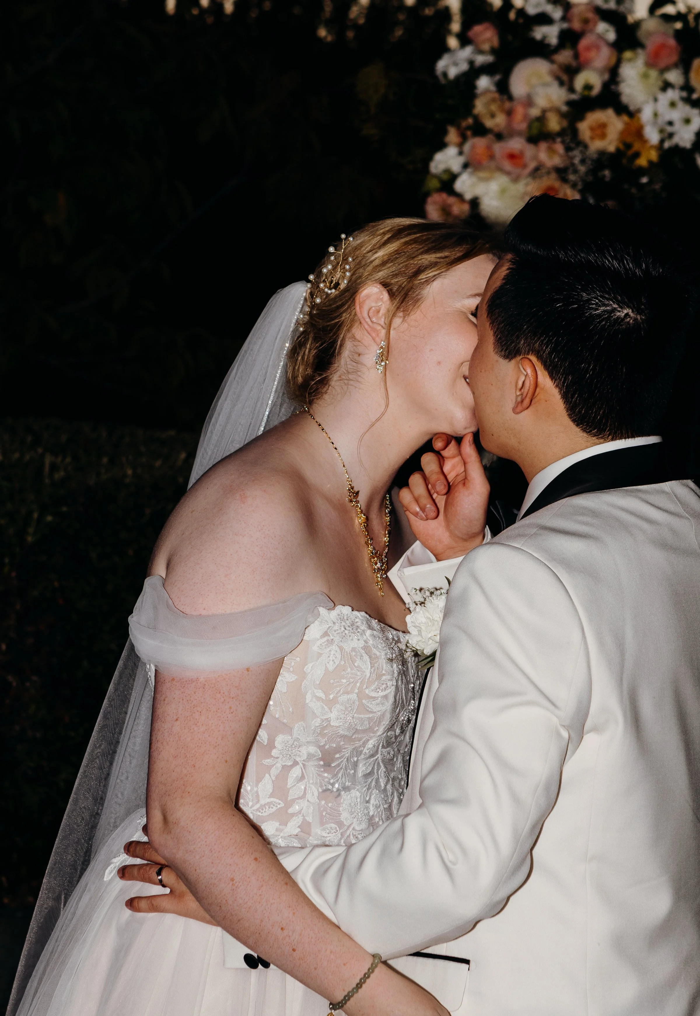 A bride and groom sharing a kiss at their wedding, with a background of flowers.