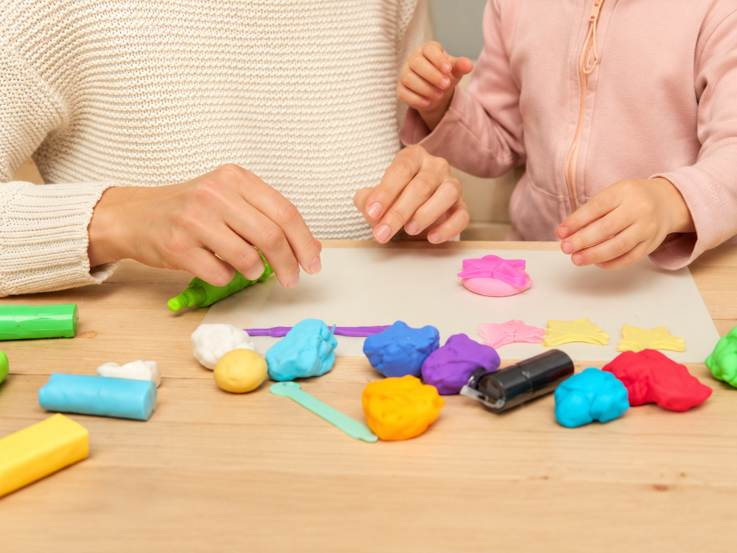 Tiener en kind maken knutselwerk met gekleurde klei en stempels, op een houten tafel.