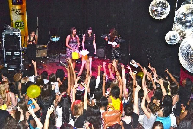 People on stage receiving awards or recognition while an audience reaches out with hands and phones in a crowded indoor event.