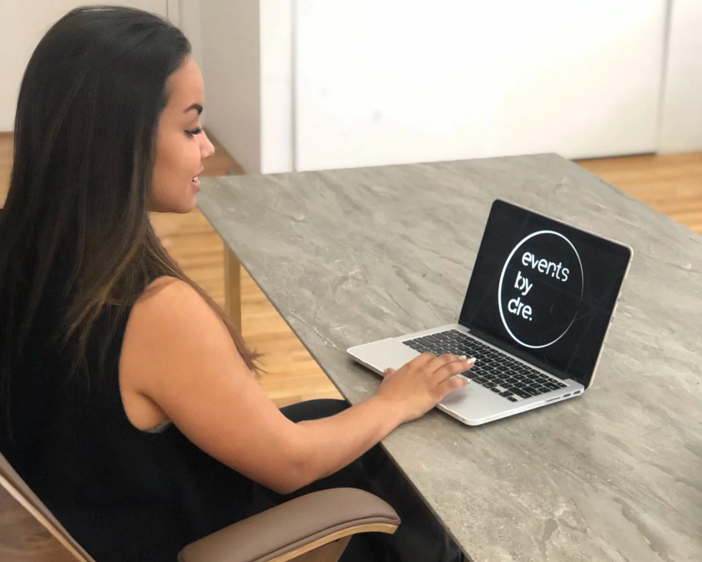 Dre, Founder of Events by Dre, sitting at a table using a laptop that displays the logo "events by dre."