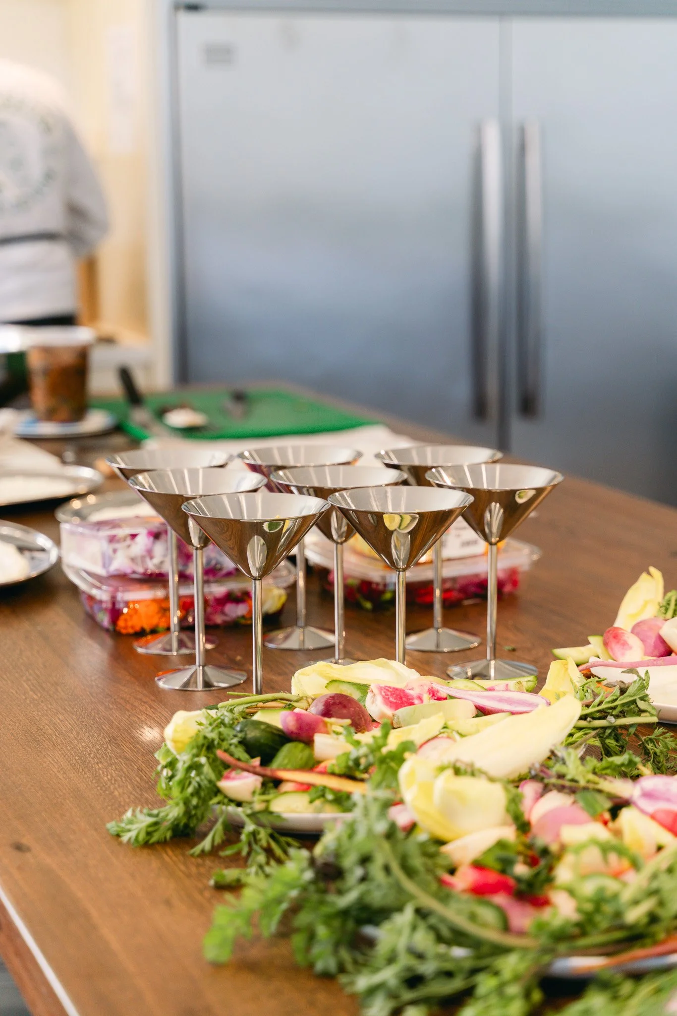 An assortment of colorful salads and empty cocktail glasses on a wooden table in a kitchen.