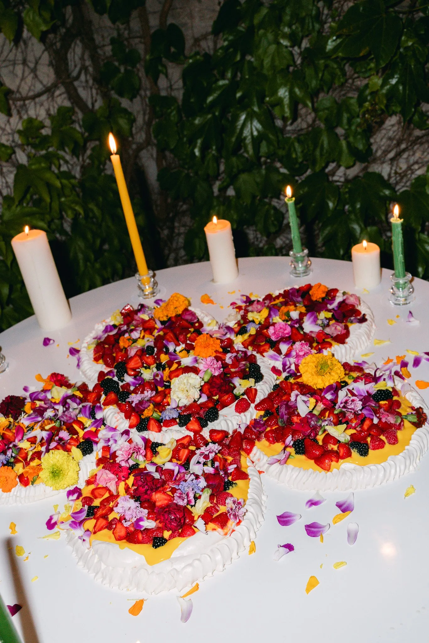 Heart-shaped fruit tart decorated with berries and flowers, surrounded by lit candles on a white table