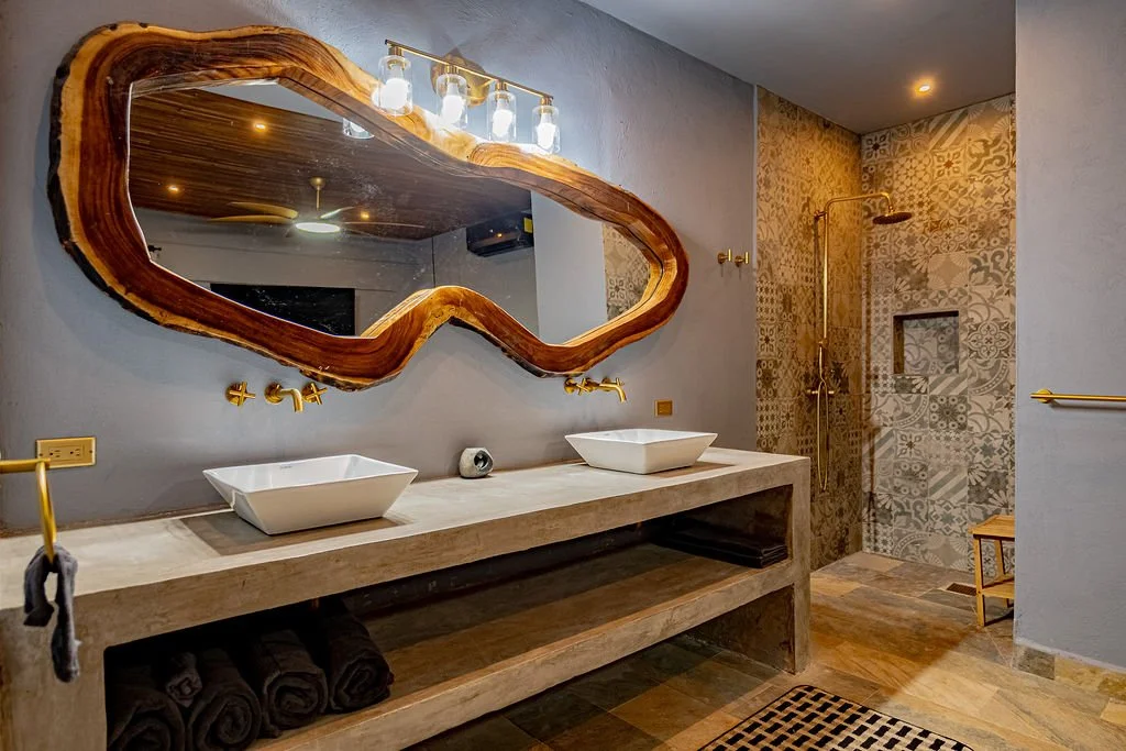 Modern bathroom with double vessel sinks, a large wooden-framed mirror, a walk-in shower with patterned tiles, and a wooden bench.