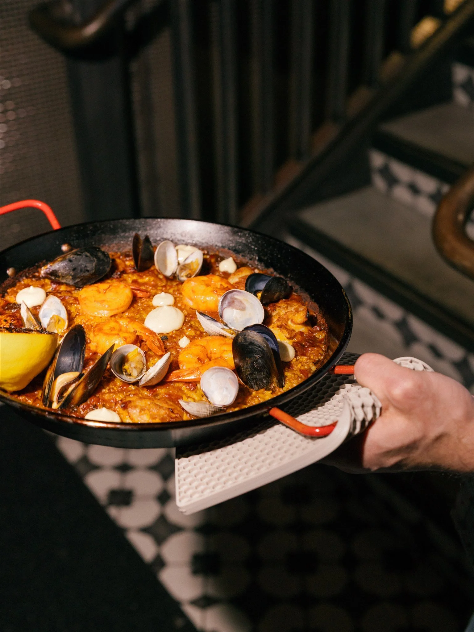 Server holding large seafood paella dish with prawns, mussels, clams and chicken.