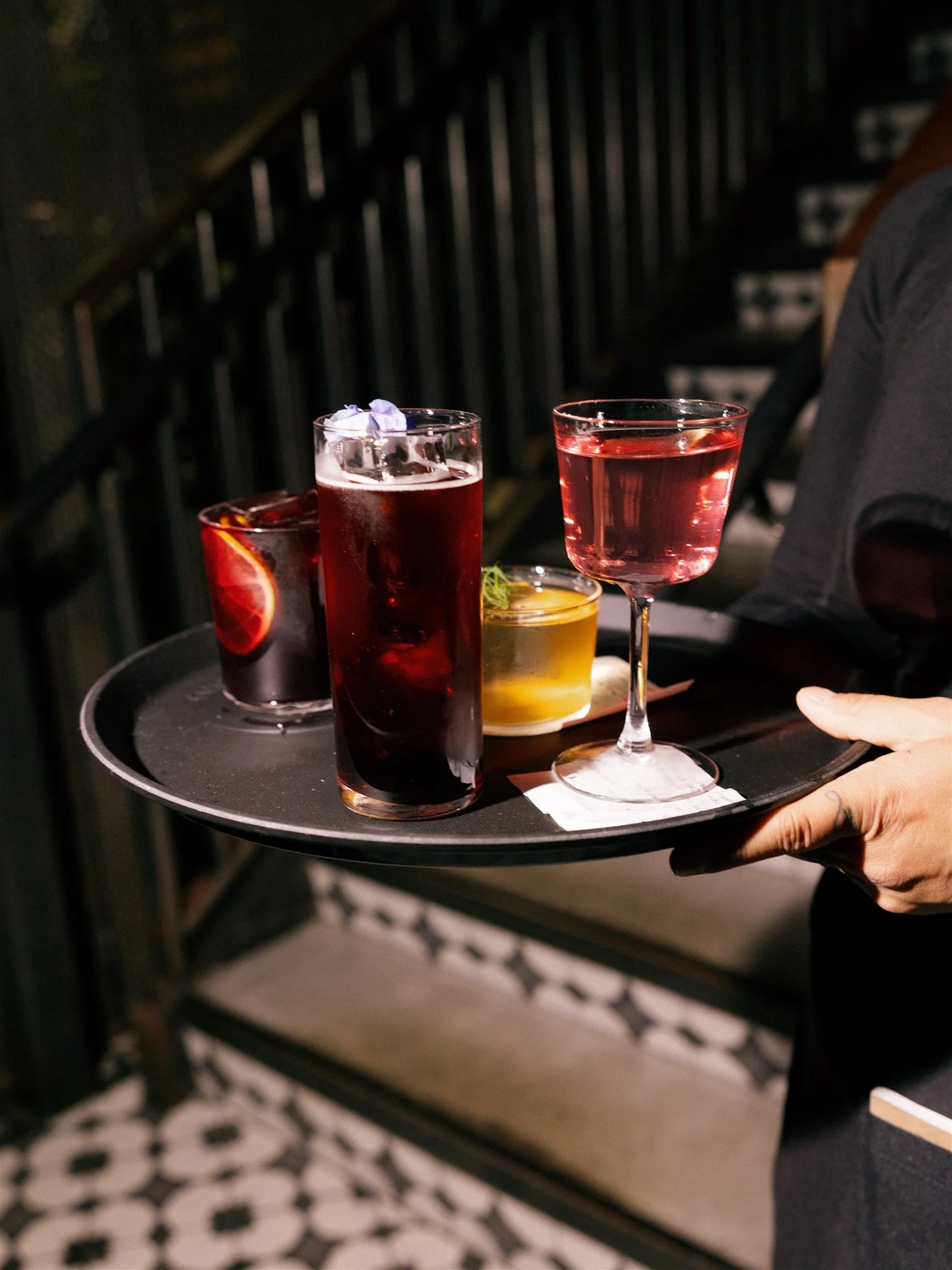 Server holding four different cocktails on a cocktail tray