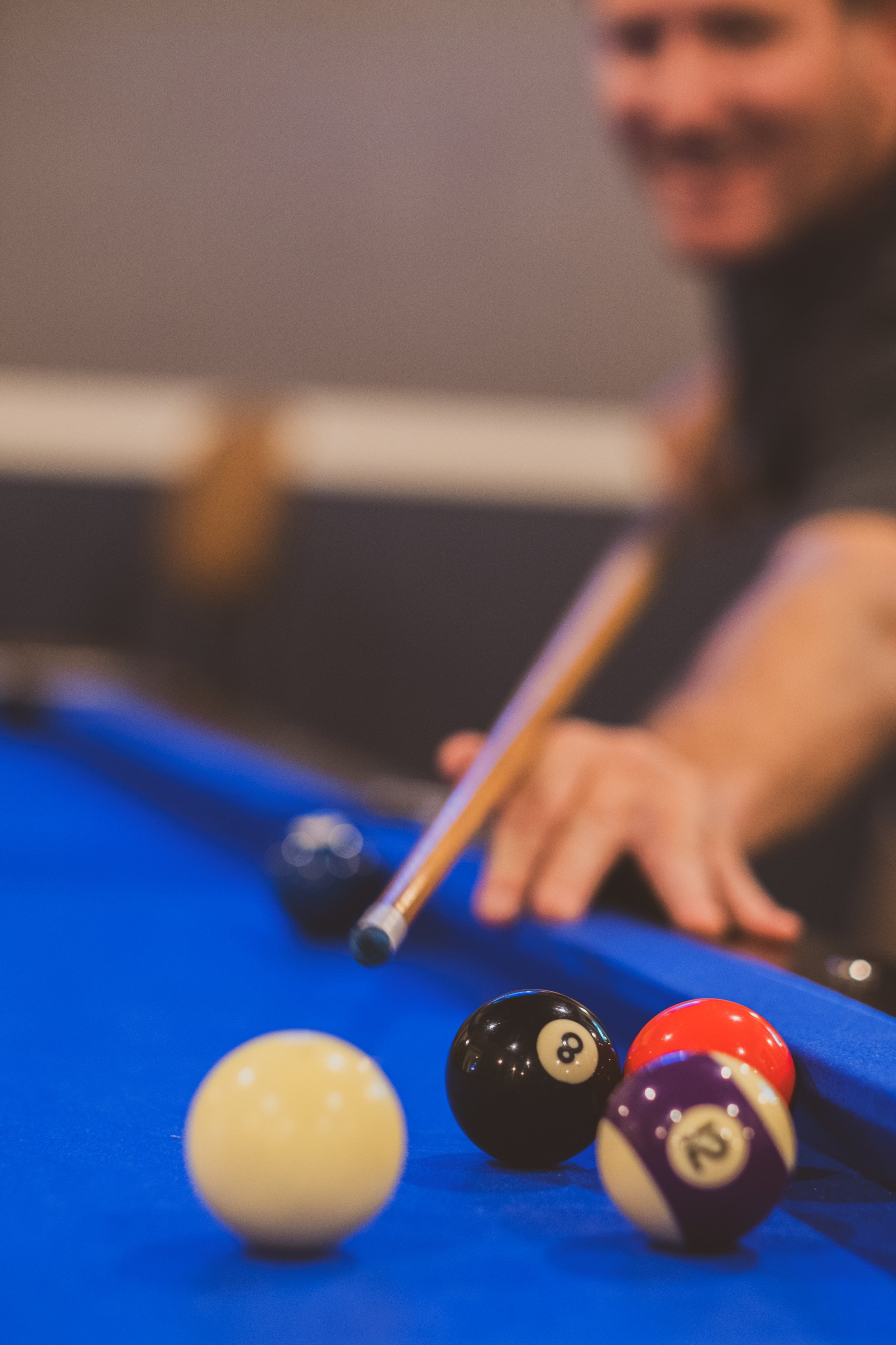 Close-up of a pool table with billiard balls at the Hastings Hotel, including the 8 ball, 12 ball, and 13 ball, with a person aiming a cue stick at the balls.