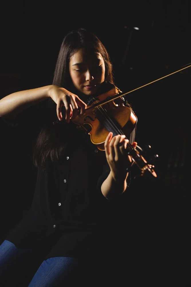 Young woman playing violin in a dark setting for Sunnyside Homeschooling's StarJam Homeschool Music Program